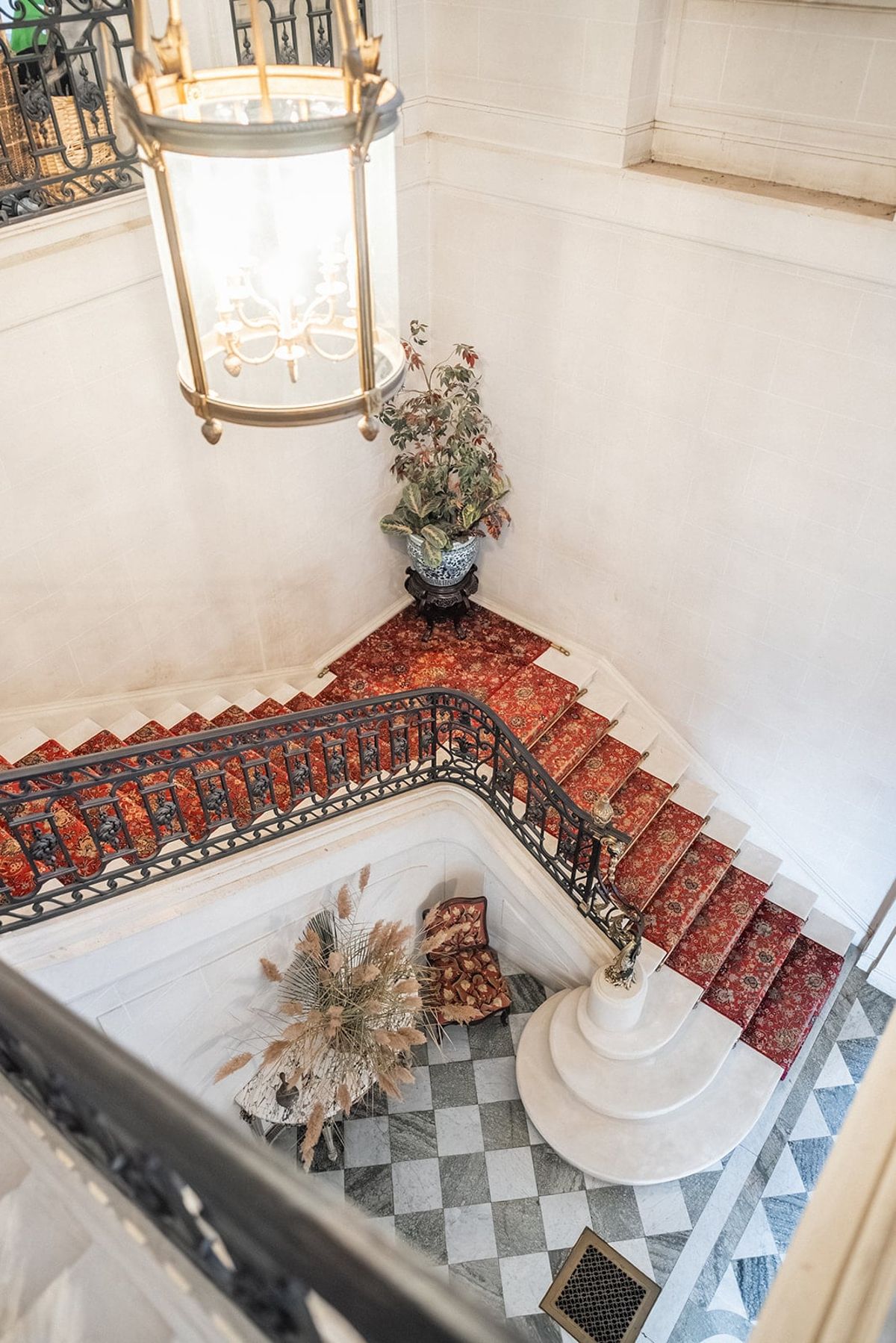 Looking down Château du Terral's carpeted staircase with iron railing, lantern and chequered marble floor
