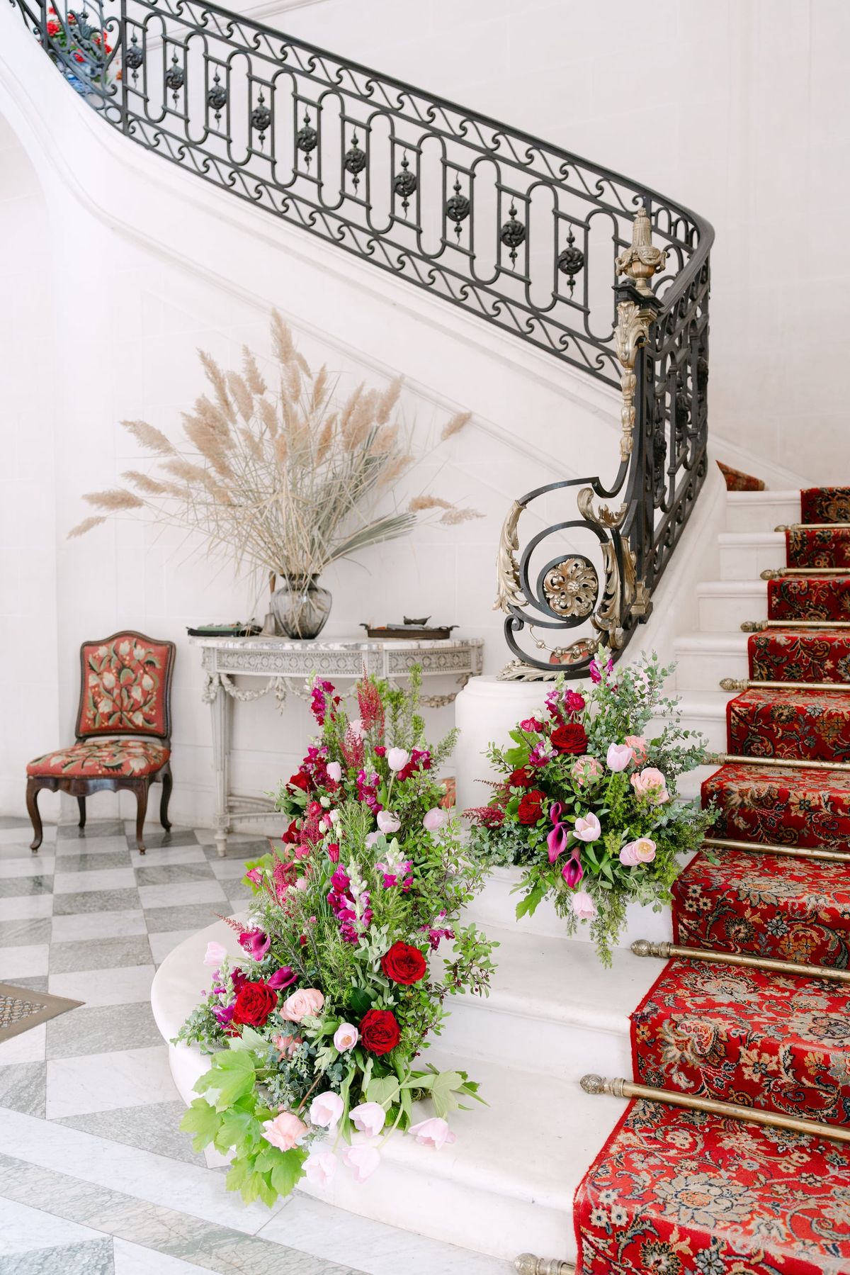 Red and pink floral arrangements on the carpeted stone staircase with iron railing at Château du Terral