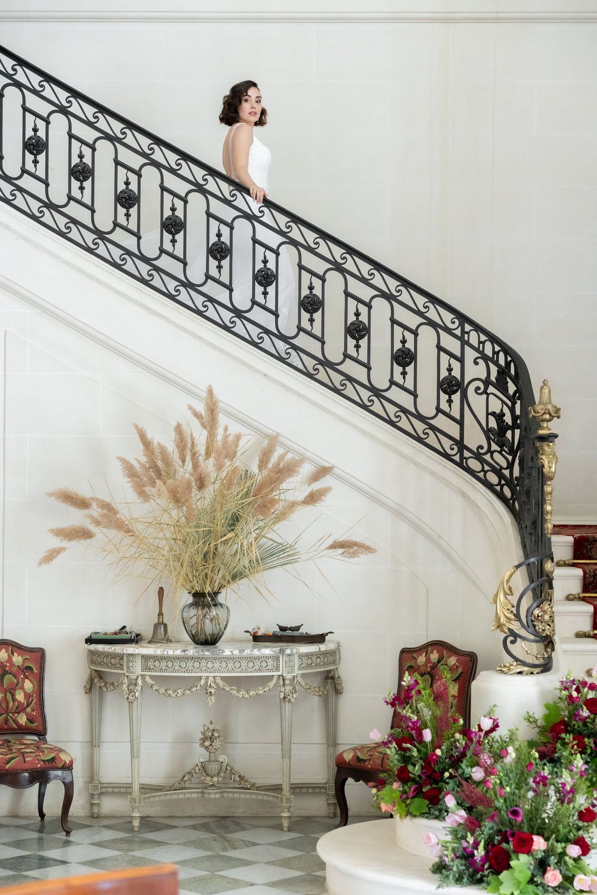 Bride atop Château du Terral's sweeping iron-railed staircase above a console with pampas grass