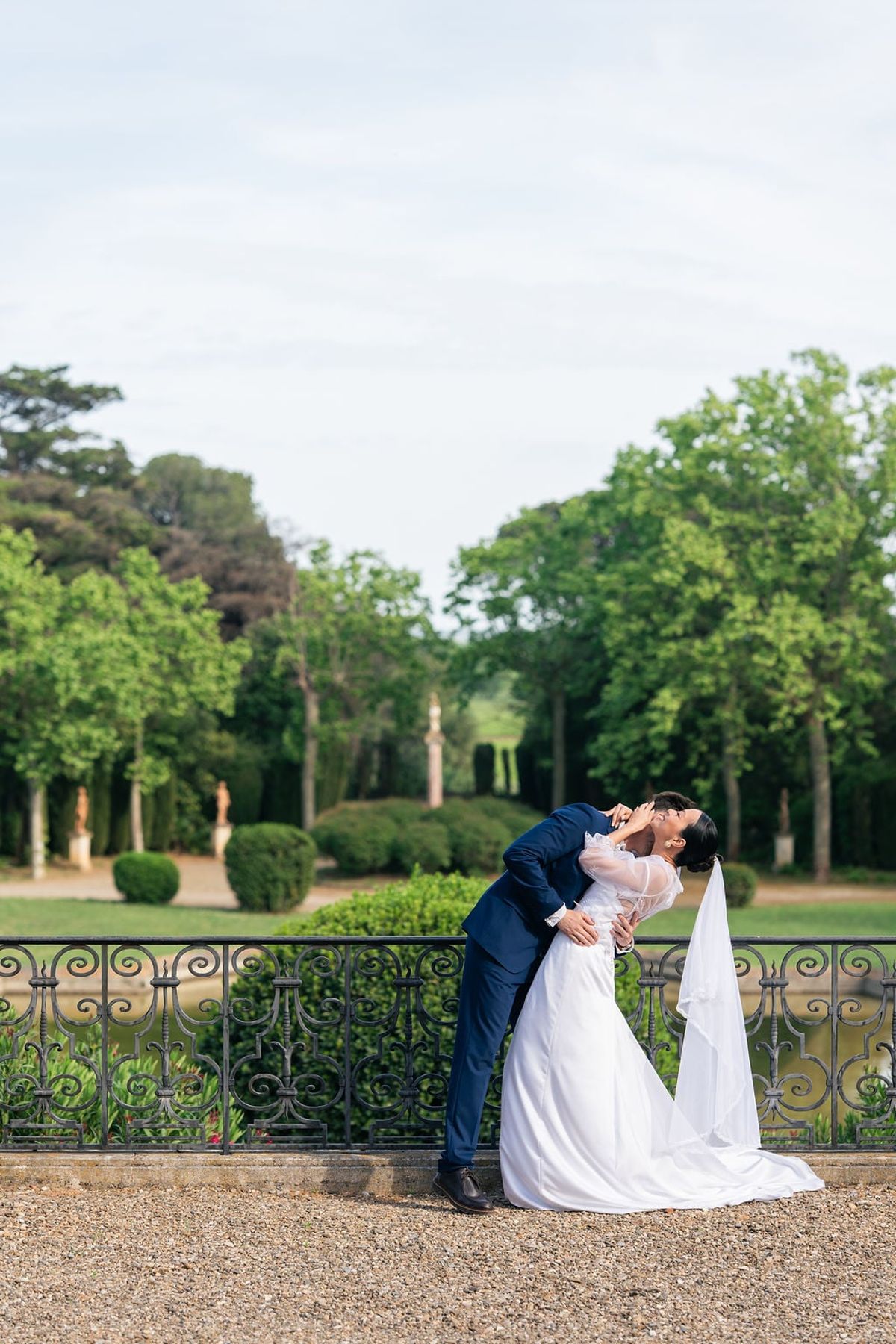 Bride and groom kissing by an ornate iron railing in the gardens of Château du Terral
