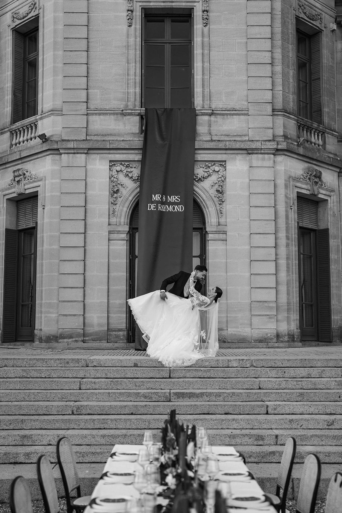 Couple on the steps of Château du Terral above a banquet table, in black and white