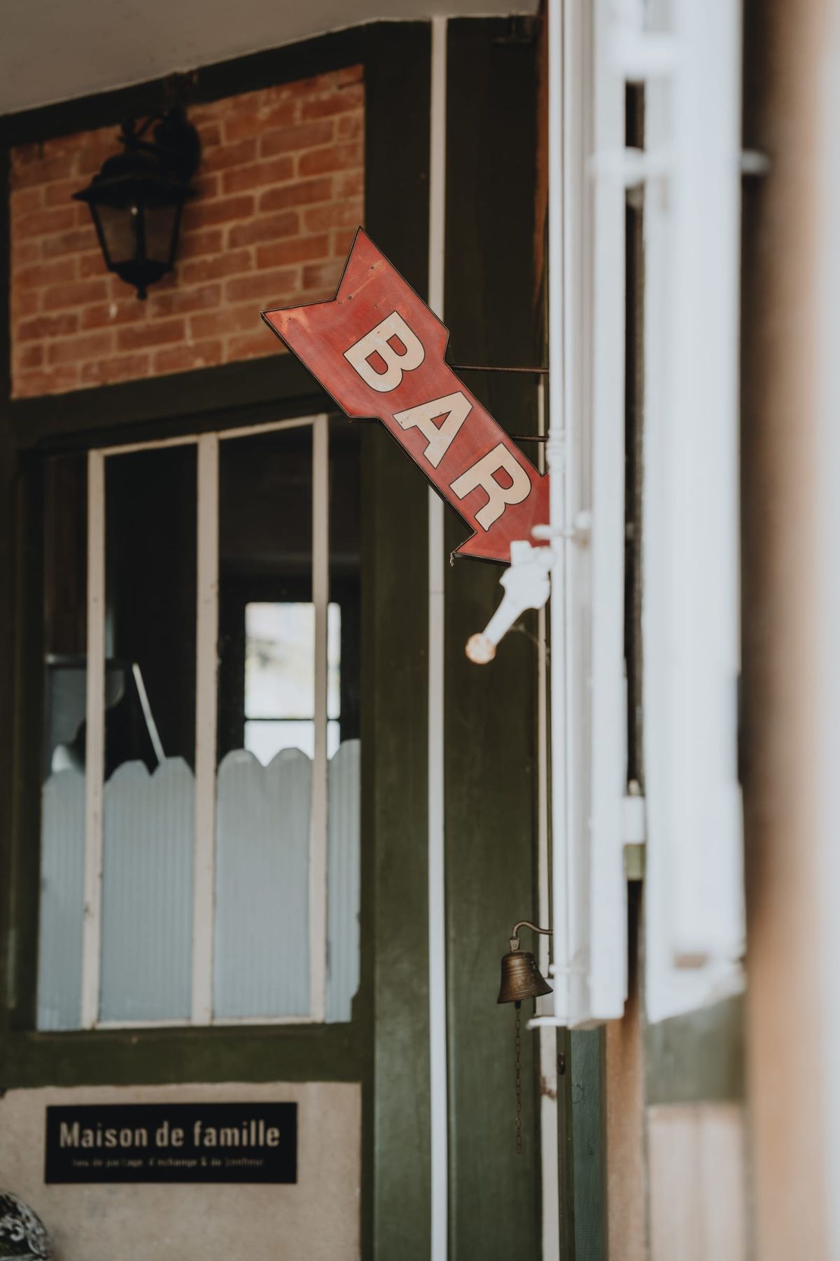 Vintage red BAR arrow sign beside a green-shuttered doorway with a hanging bell