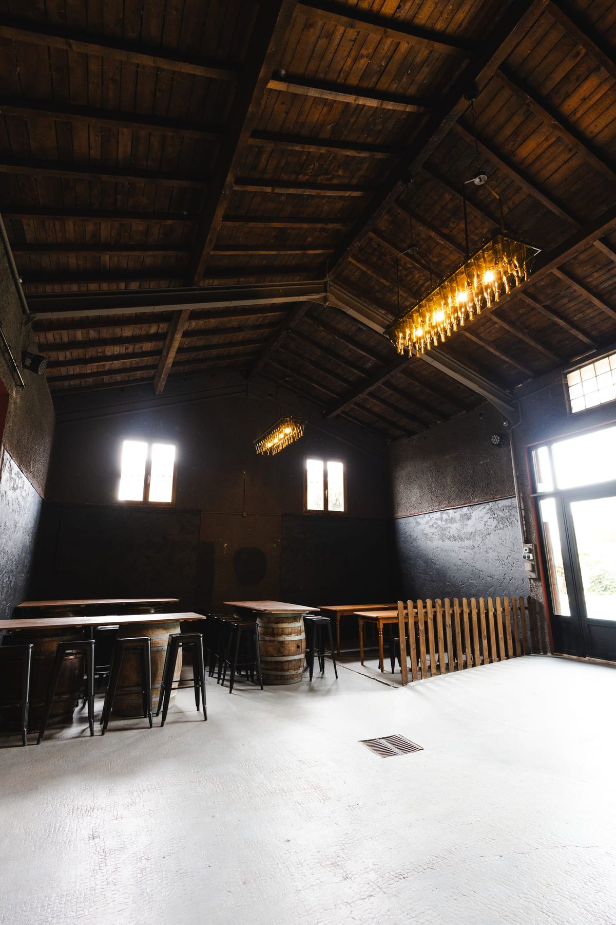 Rustic barn-style room with vaulted wooden ceiling, wine-barrel tables and tall windows