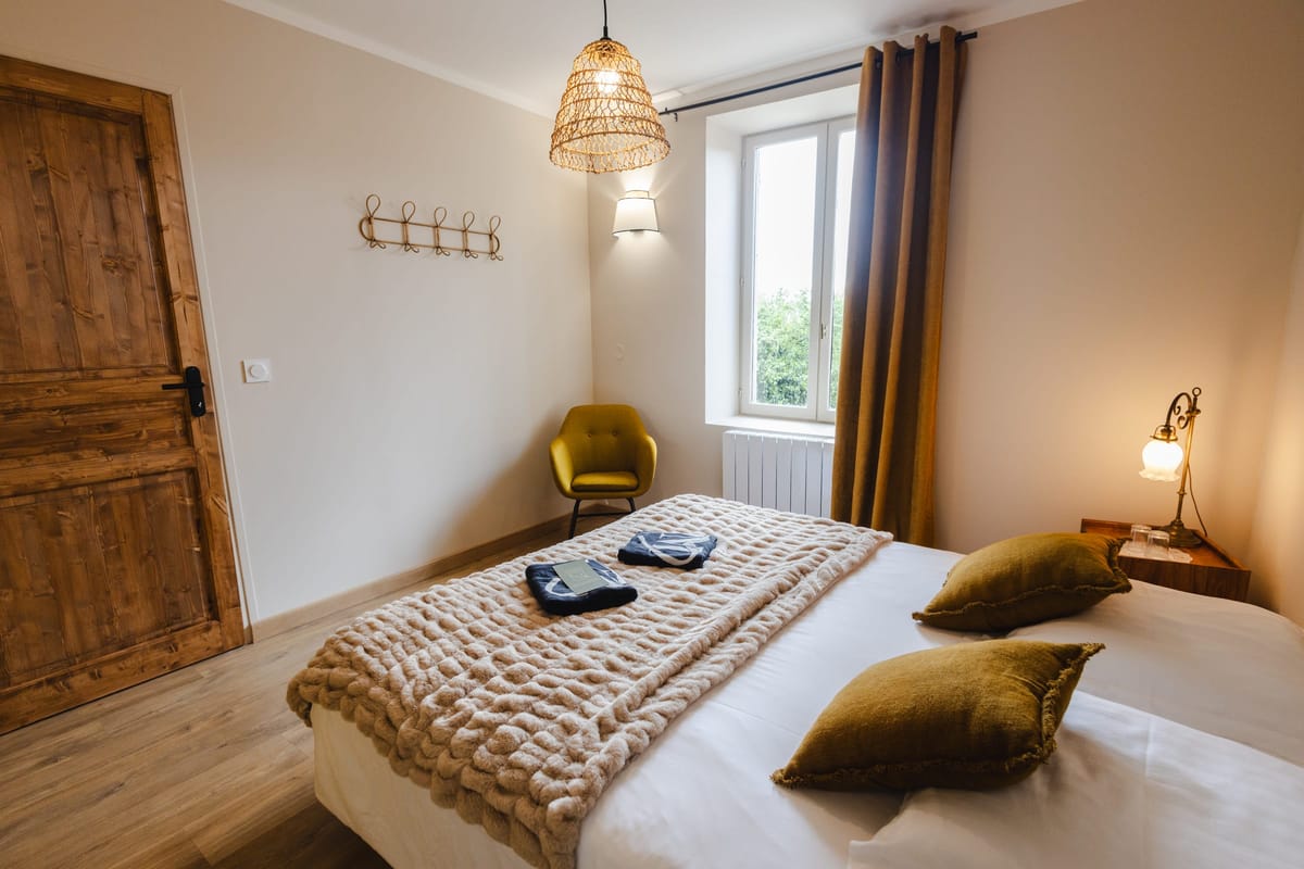 Bedroom with mustard velvet armchair, brass bedside lamp and a rattan pendant light