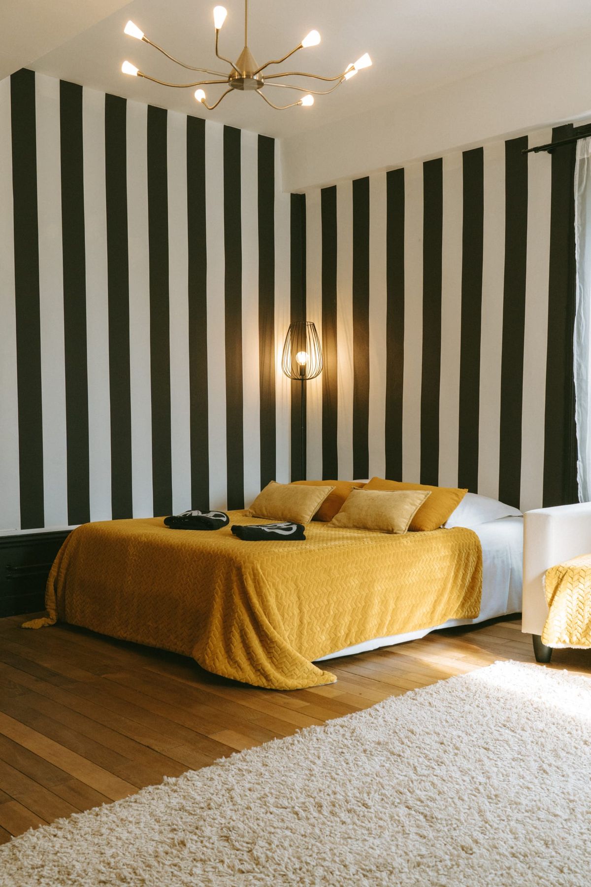 Bedroom with black-and-white striped walls, a brass chandelier and a mustard yellow bedspread