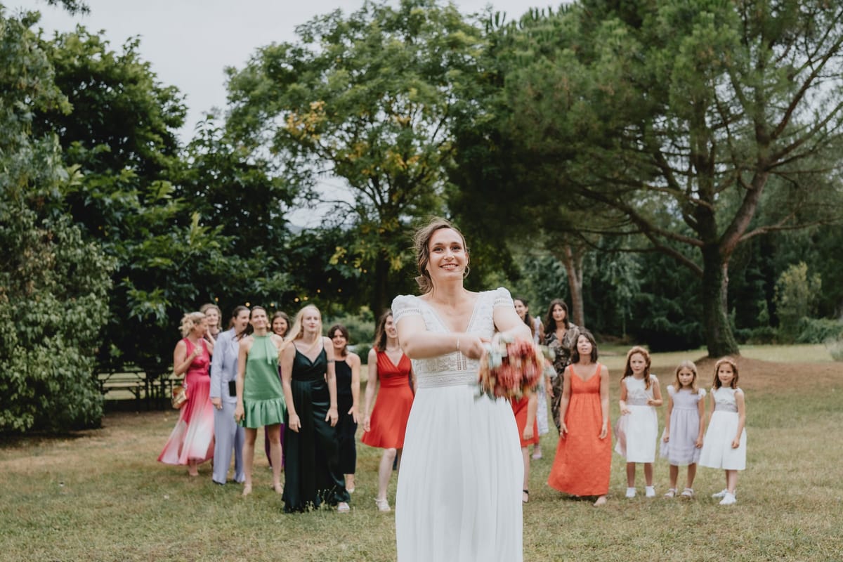 Bride tossing her bouquet to bridesmaids and guests on the lawn
