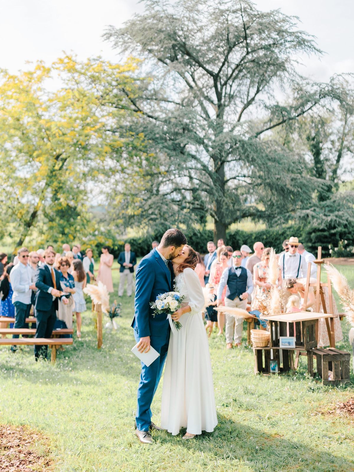 Bride and groom kissing at the outdoor ceremony with guests seated among pampas grass decor