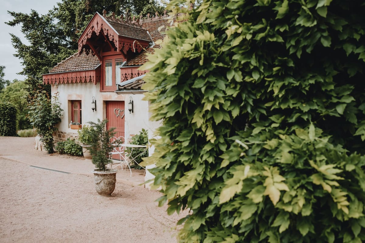 Ornate red-trimmed cottage exterior with decorative woodwork, a heart motif on the door and a small terrace
