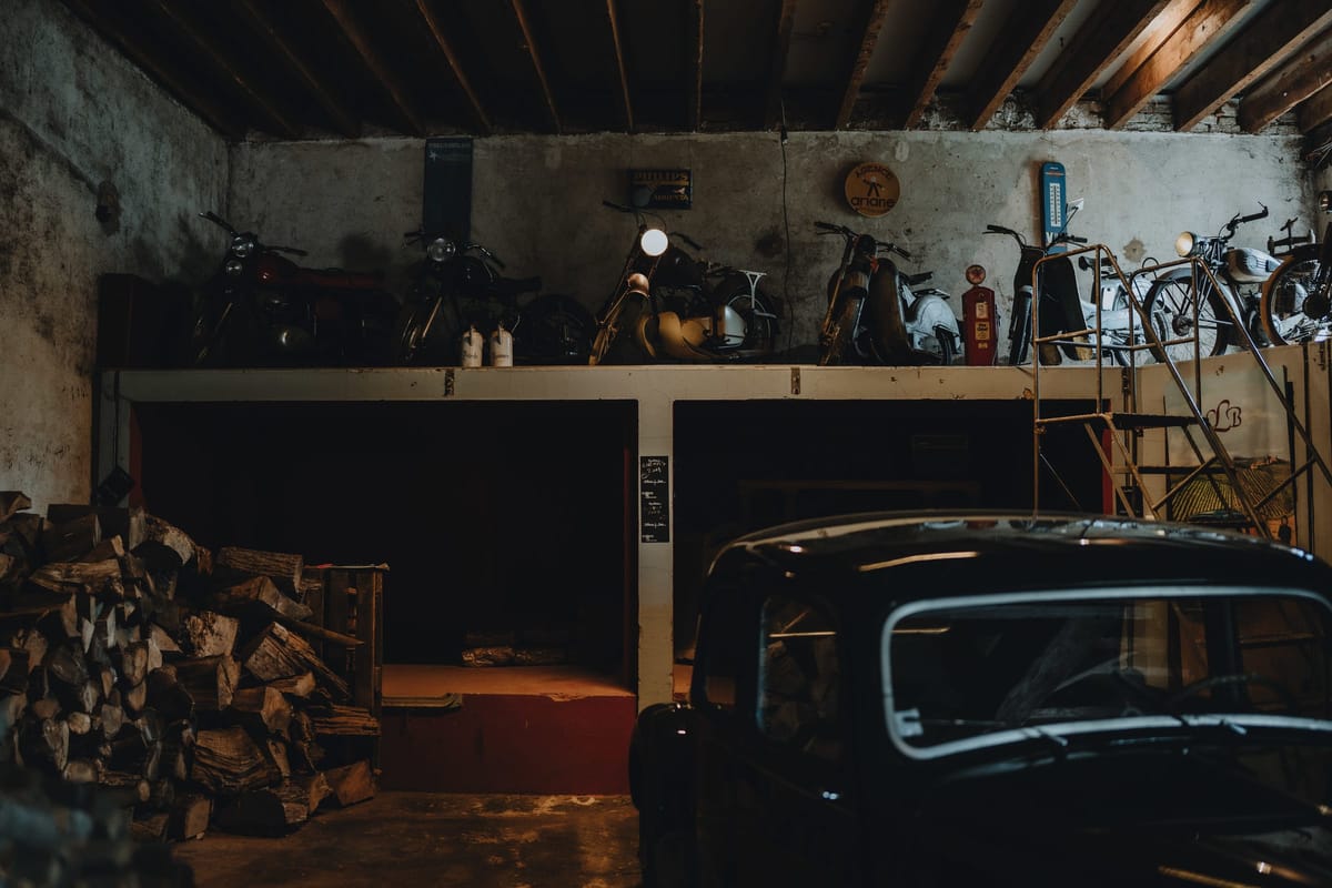 Vintage motorcycles and a classic car displayed on a raised platform in a stone outbuilding