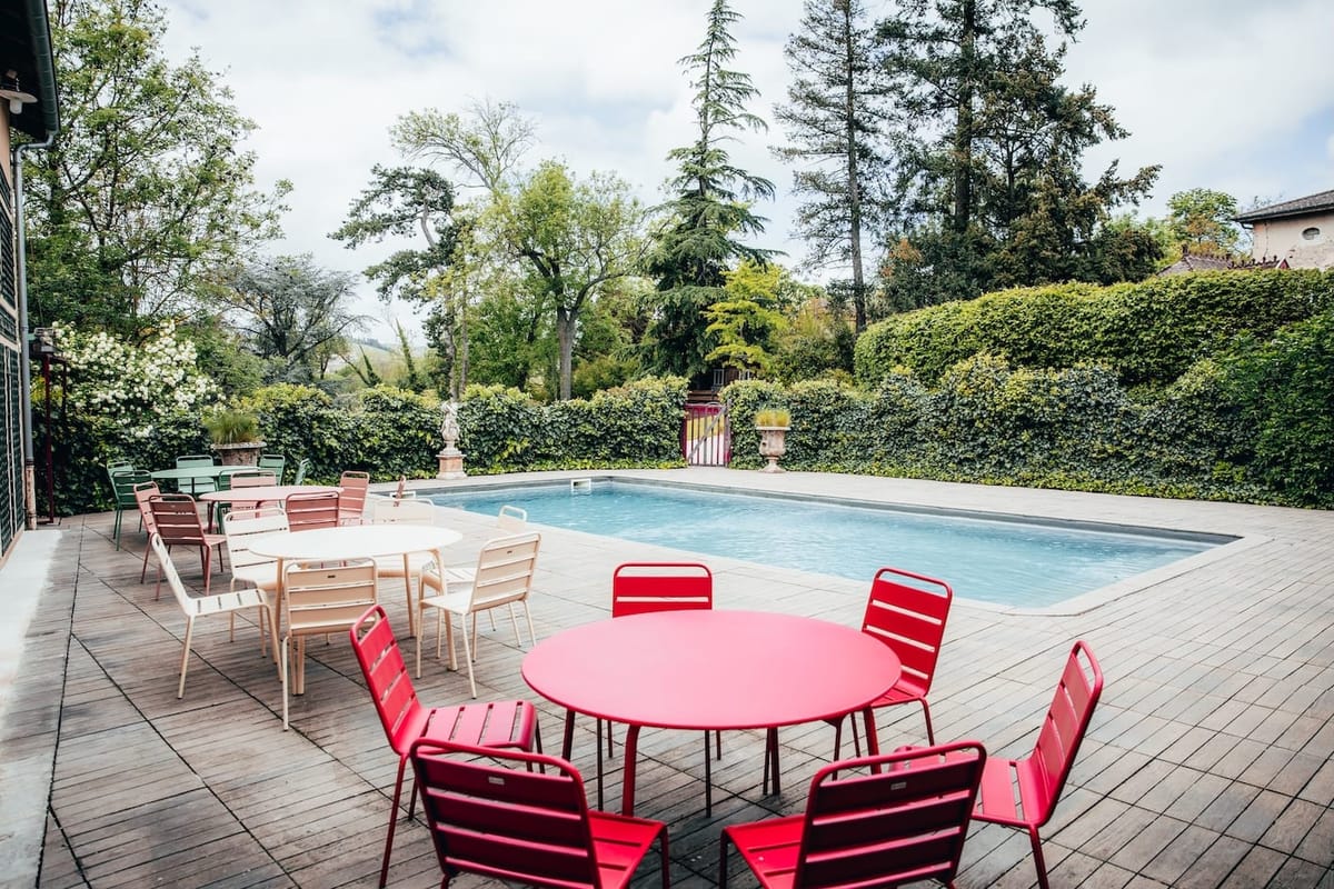 Poolside terrace with colourful bistro tables and chairs, ivy hedge and statue behind