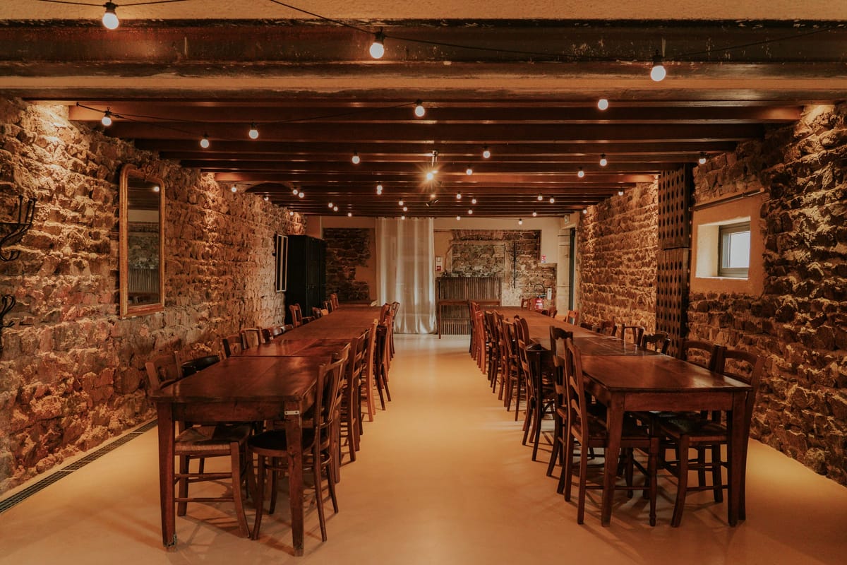 Salle Fleur de Lys stone cellar set for dinner with long wooden tables and festoon lighting