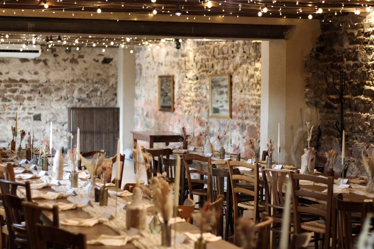 Wide view of Salle Fleur de Lys set for dinner, exposed stone walls strung with festoon lights