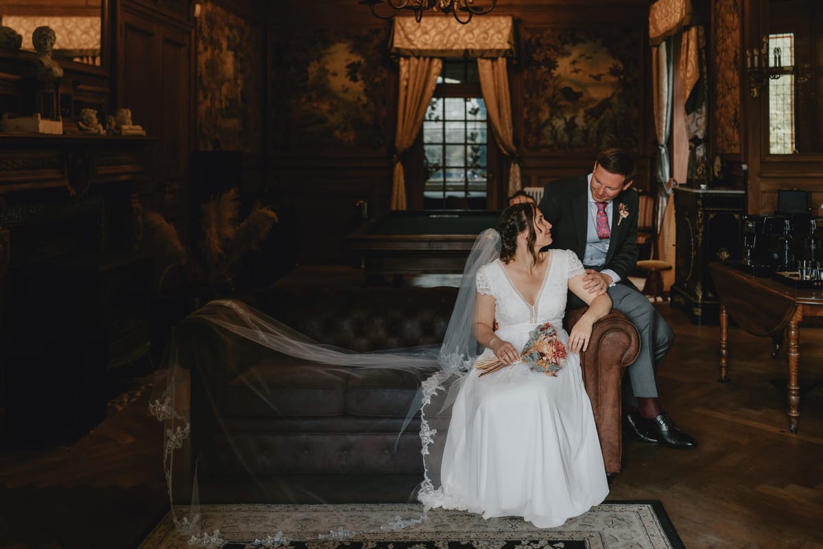 Bride and groom seated together on a leather sofa in the wood-panelled salon
