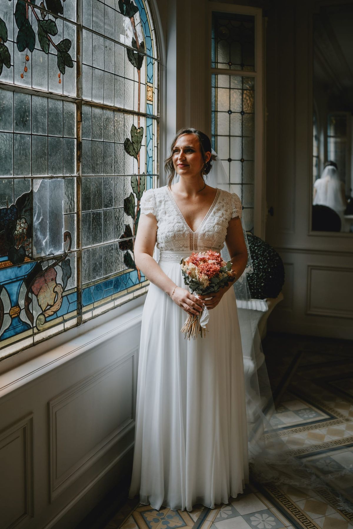 Bride standing by a stained-glass window holding her bouquet