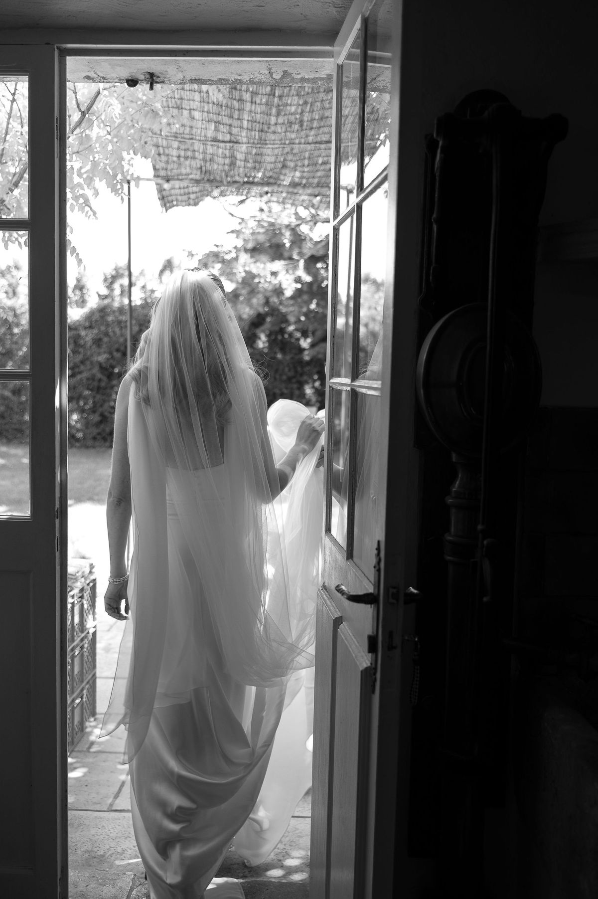 Black and white portrait of Louise in her silk gown and veil stepping through a doorway