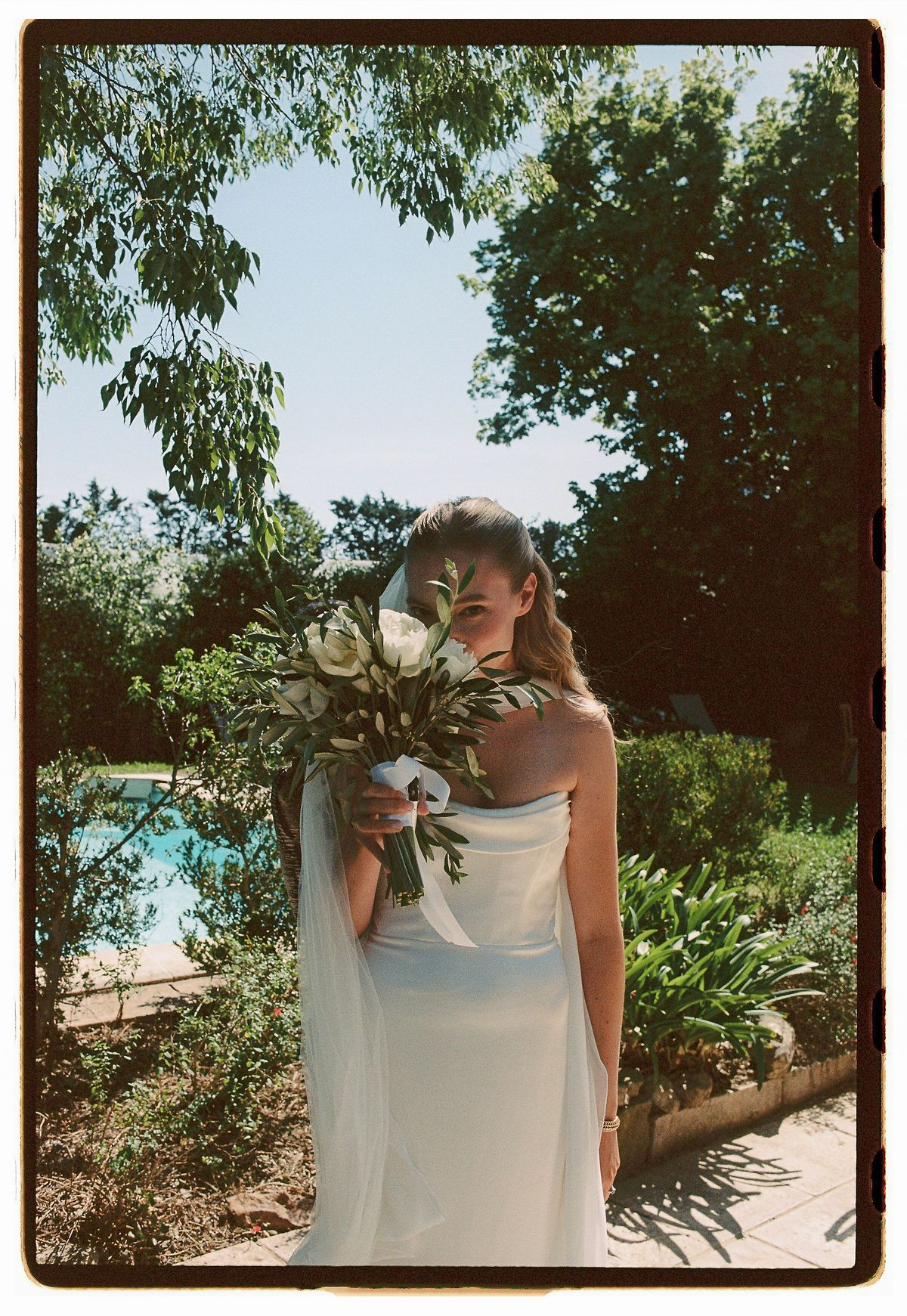 Louise holding her white and green bouquet in the garden, photographed on film