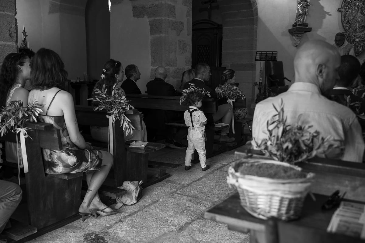 Black and white photograph of guests seated in the church with olive branches tied to the pews