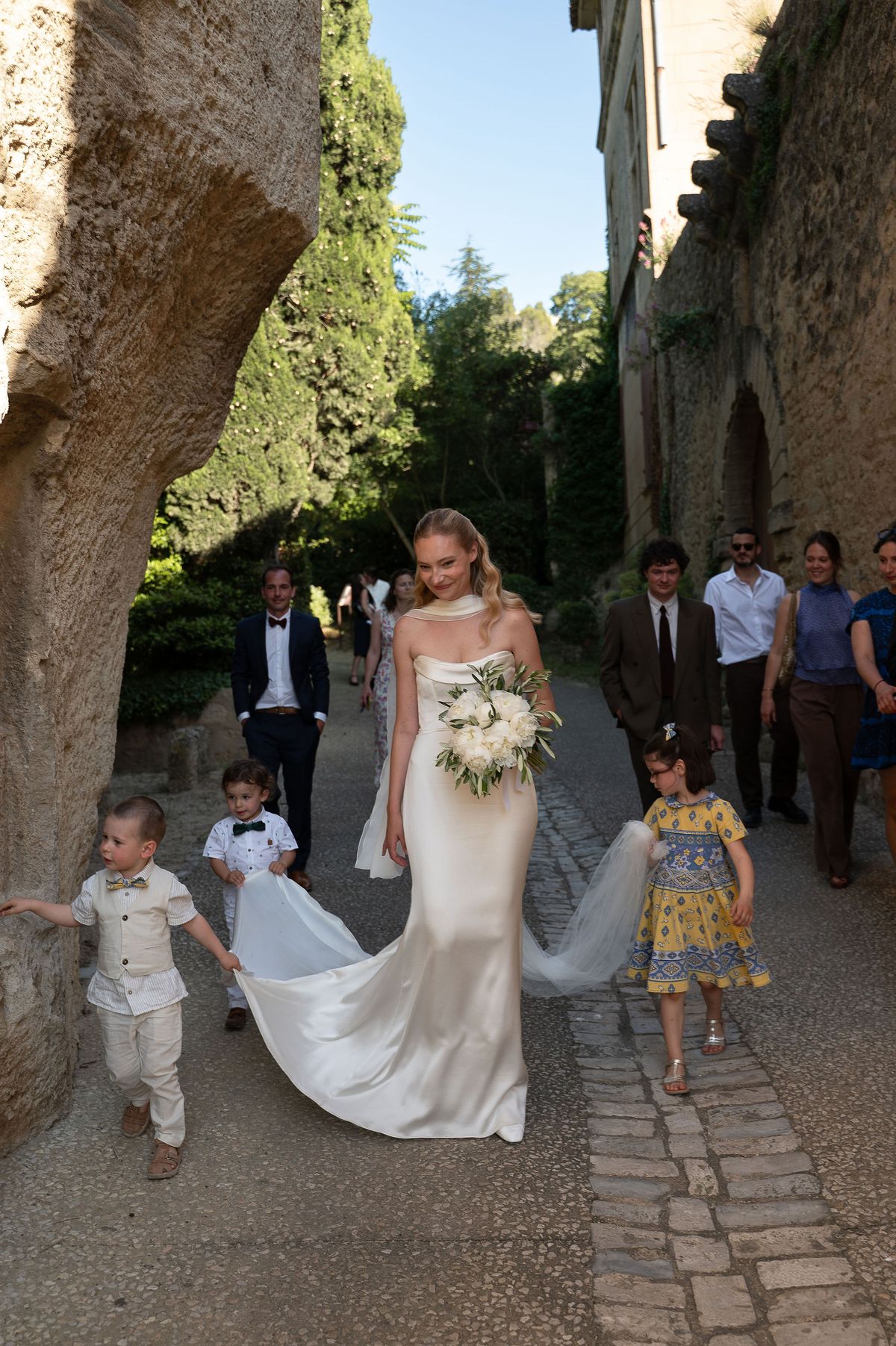 Louise and Lucas walking down the village lane with children carrying her veil