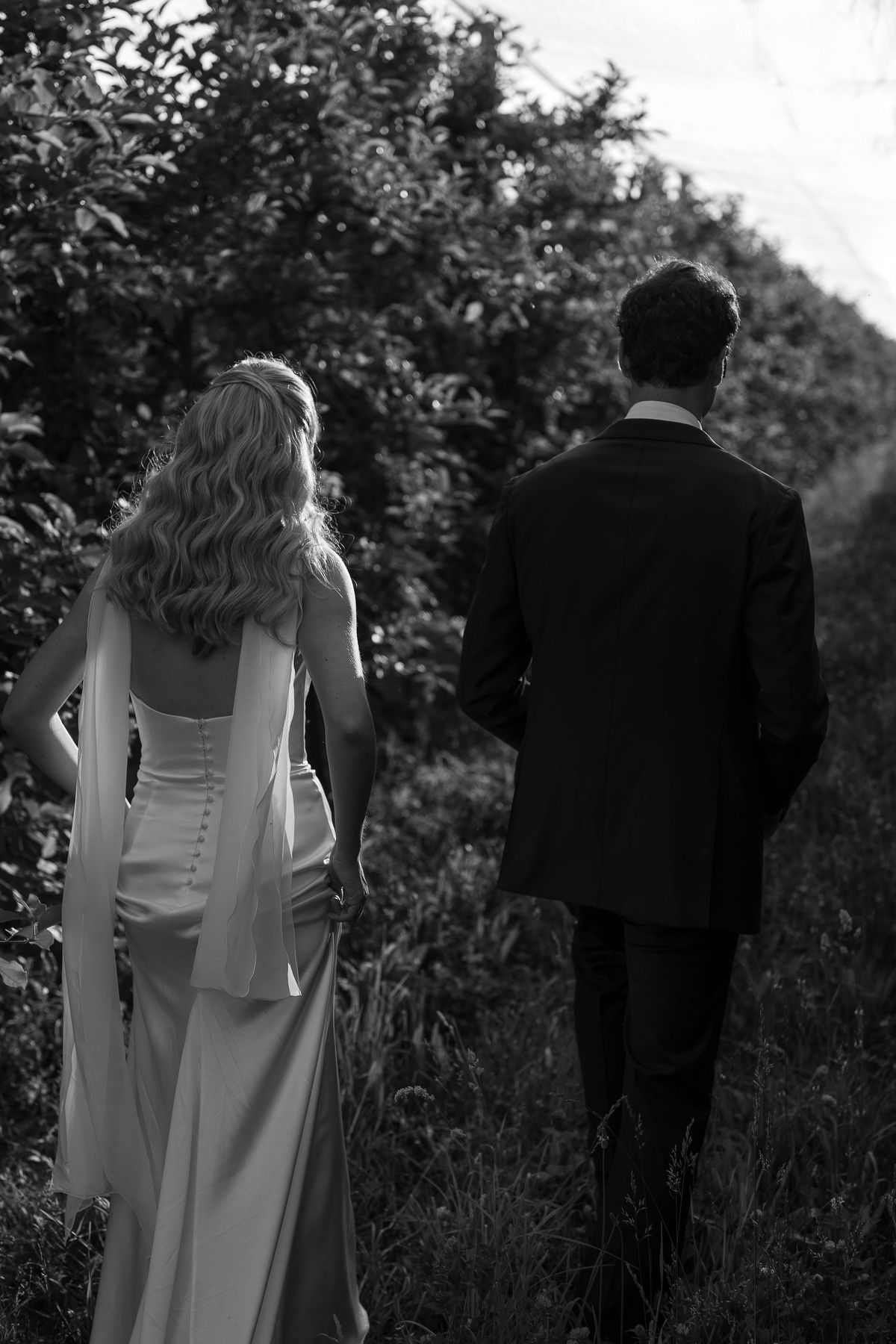 Black and white photograph of Louise and Lucas walking away through the orchard