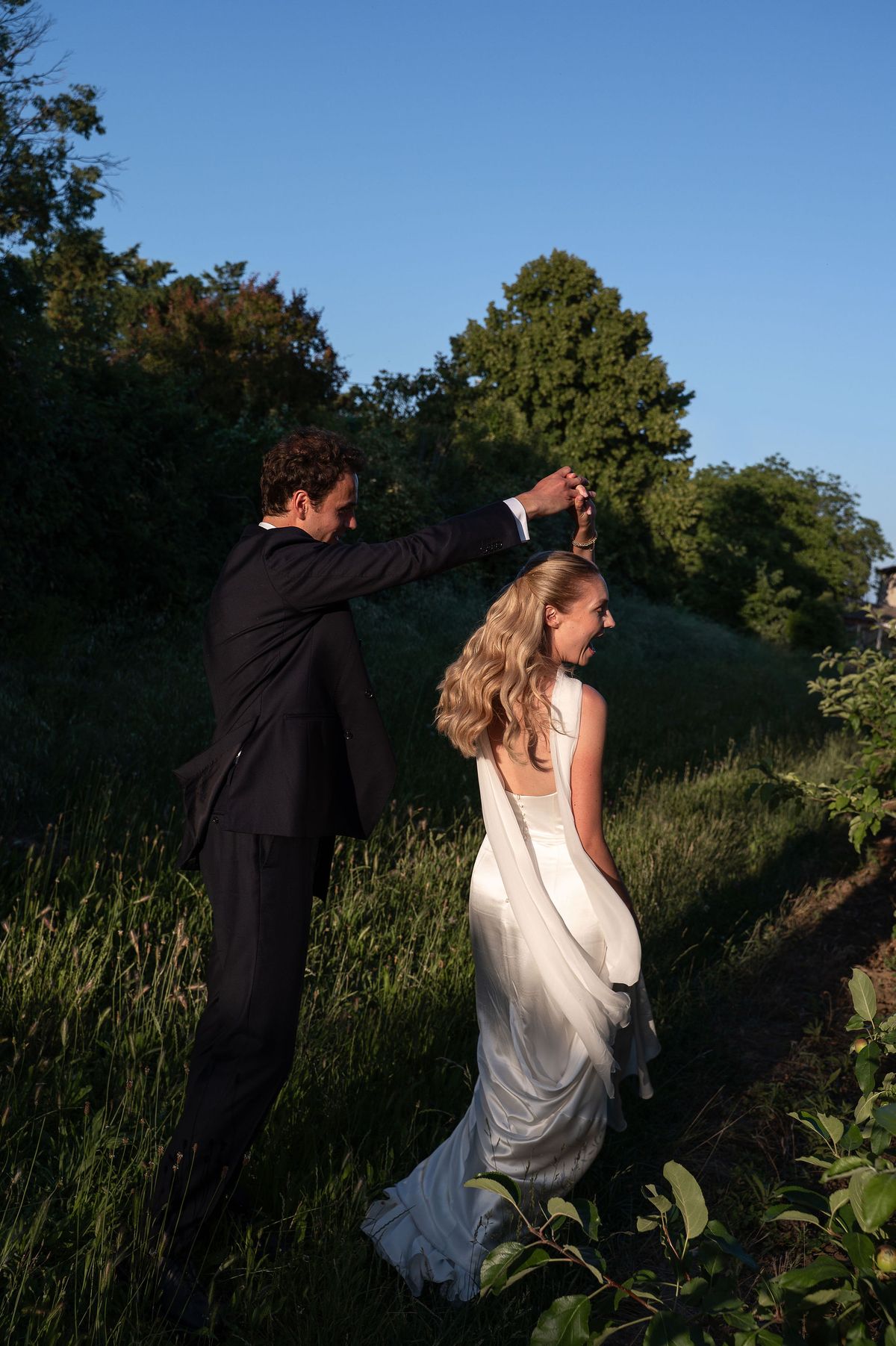 Lucas lifting Louise's hand as they turn together in the orchard grass