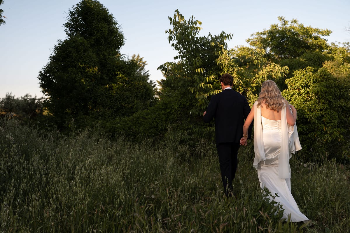 Louise and Lucas walking hand in hand through the orchard grass in the evening