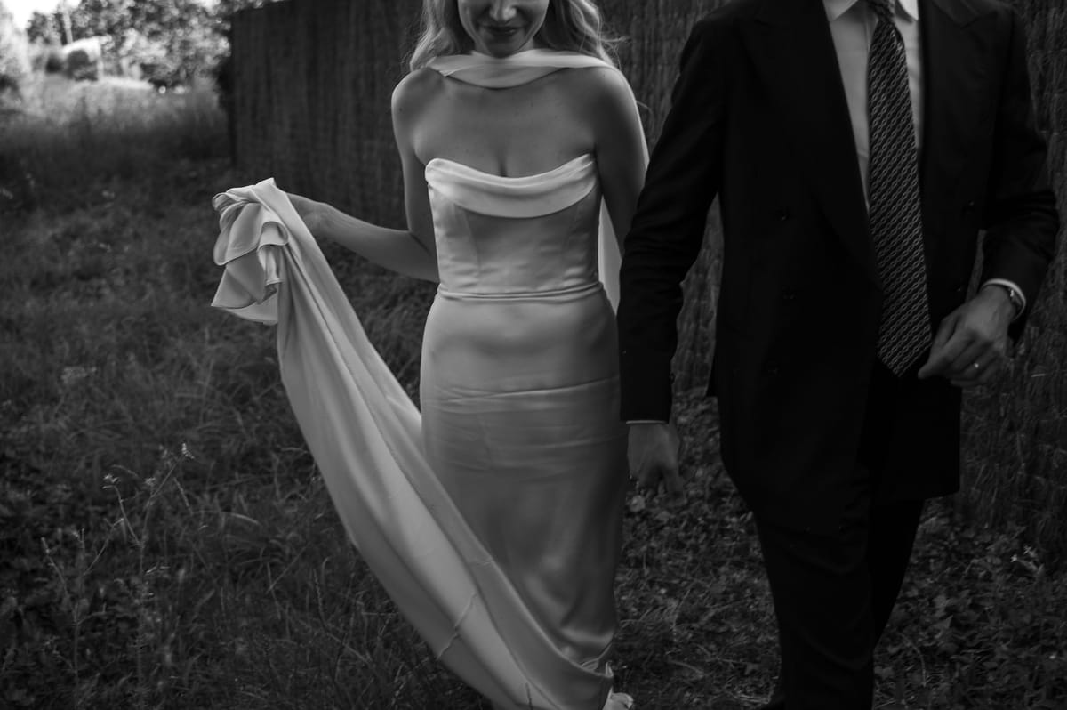 Black and white photograph of Louise holding her silk train as she and Lucas walk