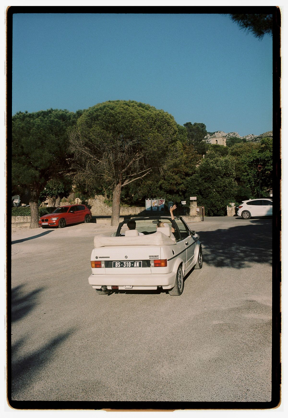 A vintage convertible parked beneath a pine tree, photographed on film