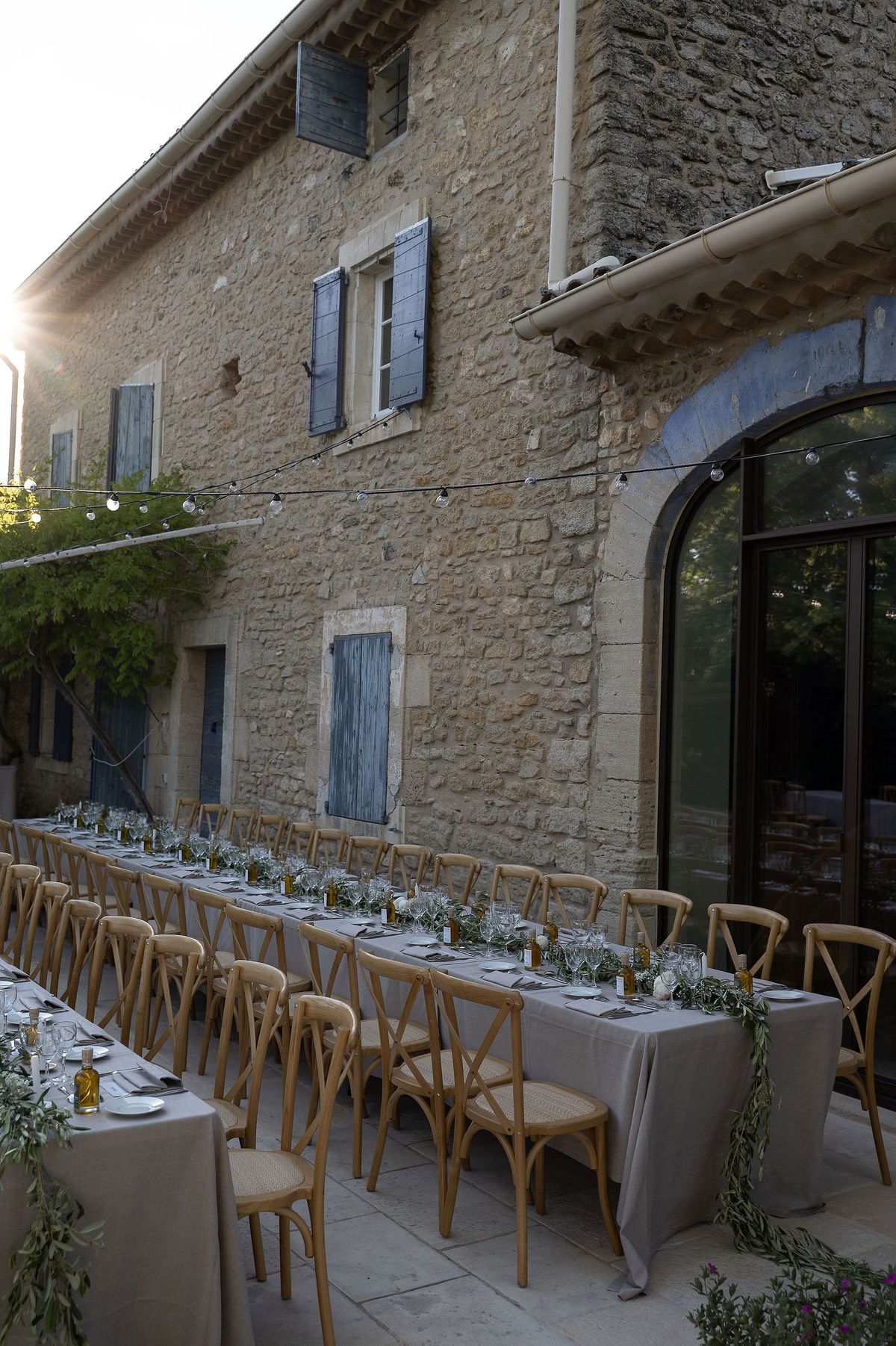 The long reception table set with olive branches and candles against the stone family home