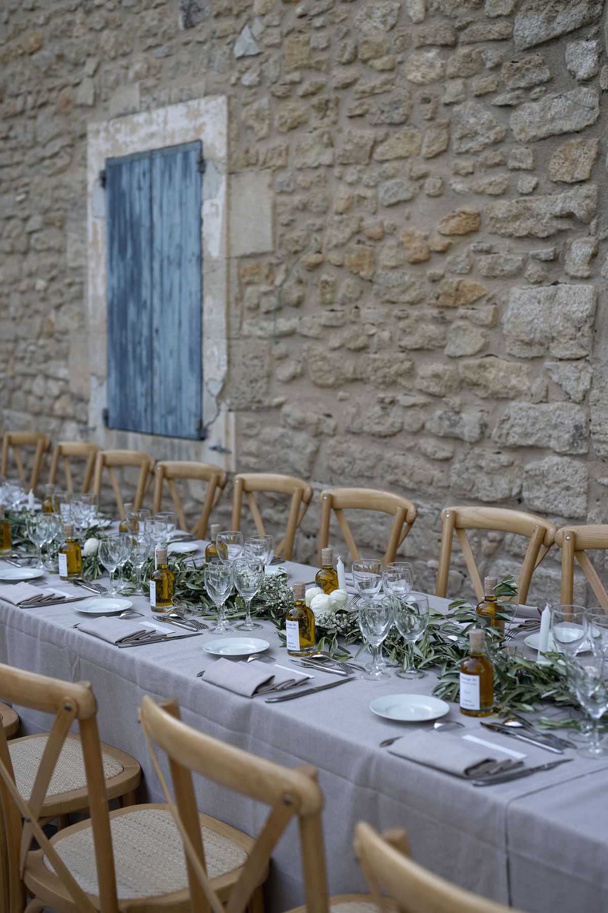 Reception tables set with linen, candles and olive branches beside a Provencal stone wall