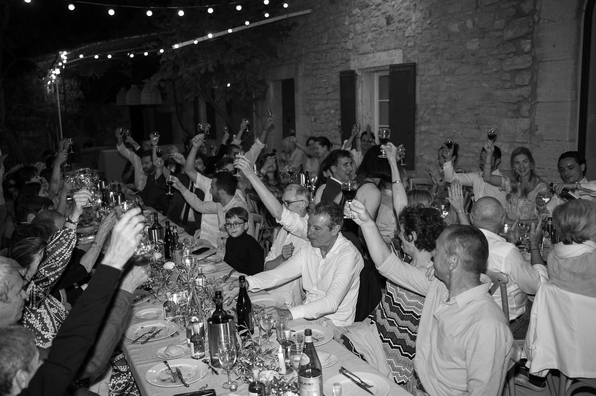 Black and white photograph of guests raising their glasses in a toast at the long table