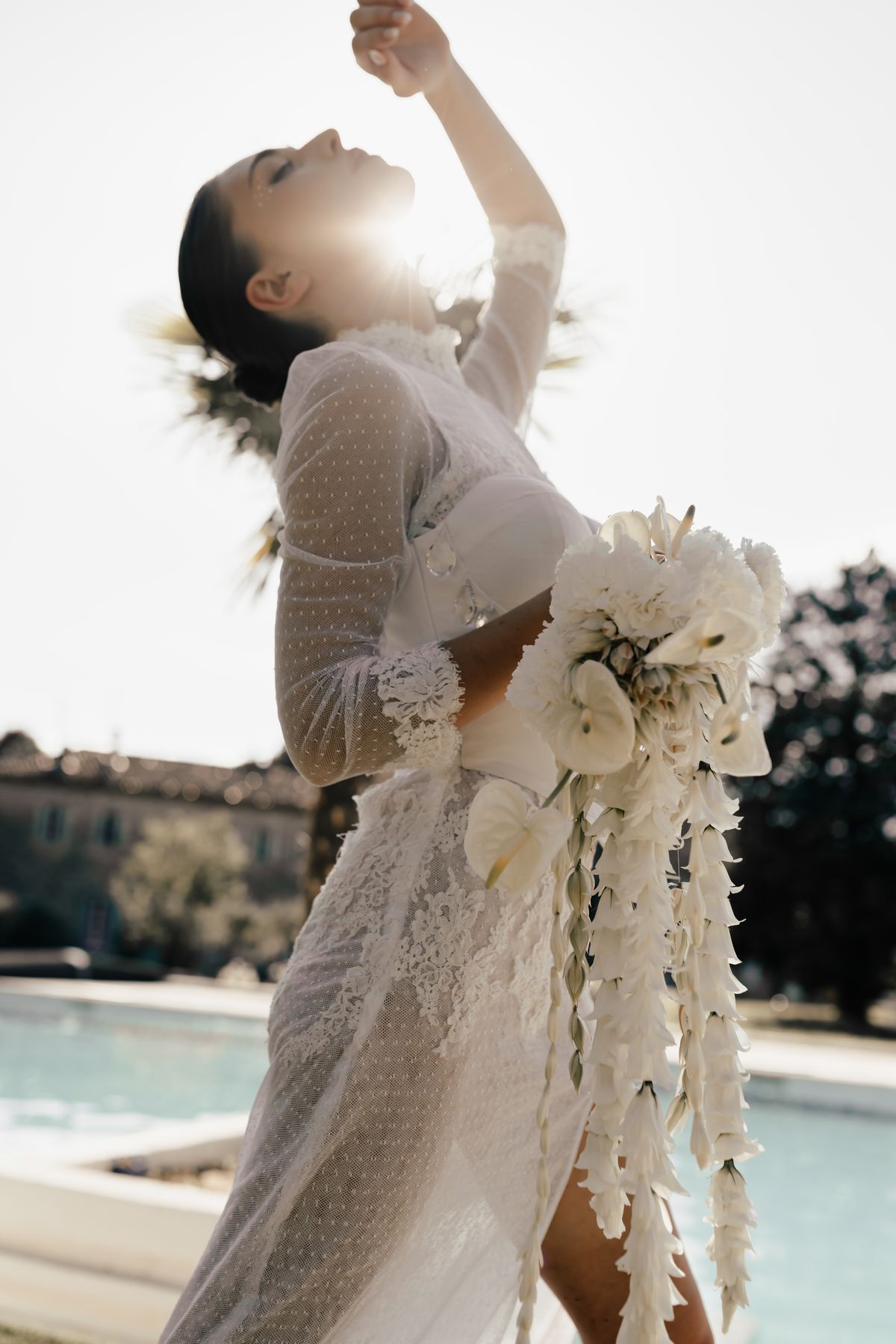 Bride with one arm raised holding a trailing bouquet at the poolside