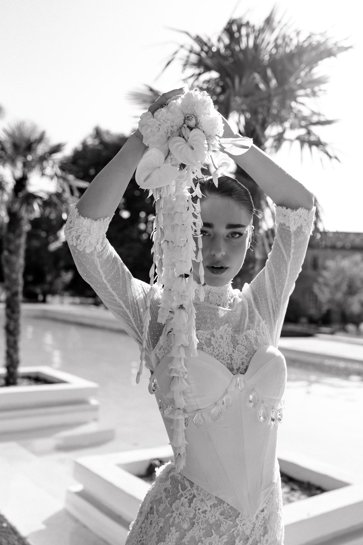 Black and white portrait of the bride with both arms raised, florals in her hands