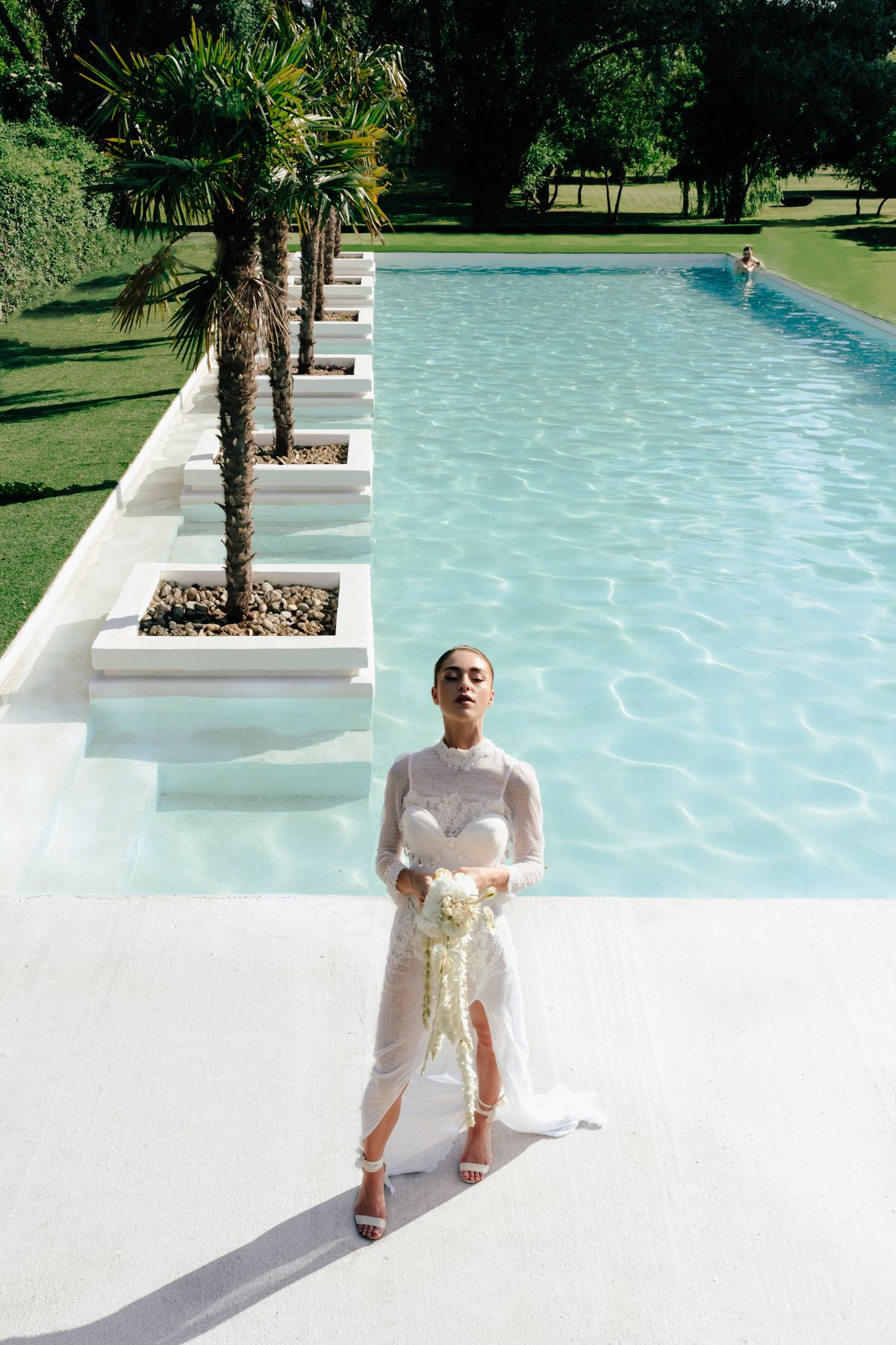 Bride standing beside the pool with palms and cypress behind her