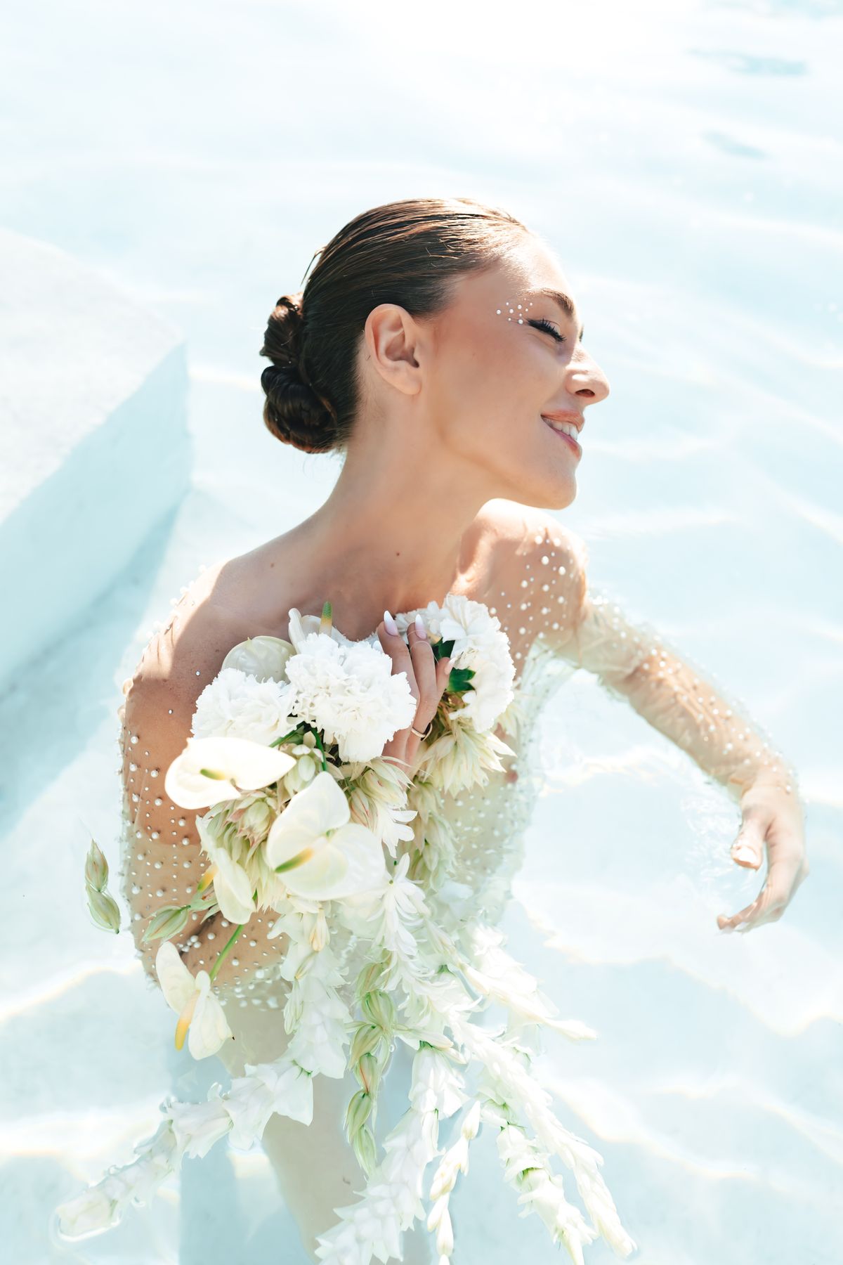 Bride in the pool with her head tilted back, florals held at her shoulder