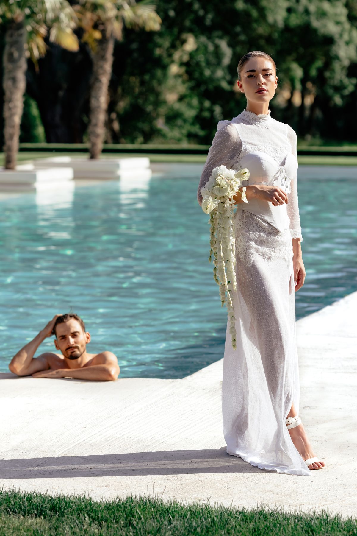Aure & Leo at the poolside, one reclining on the terrace and one standing in a long white gown