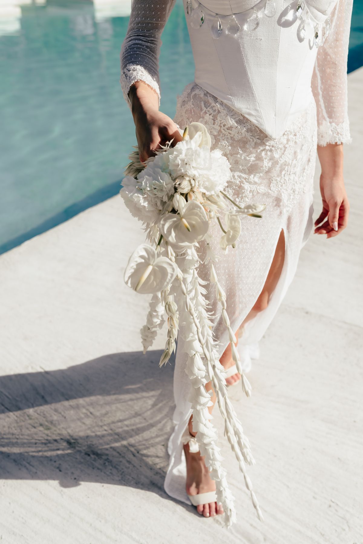 Detail of the lace gown and trailing bouquet as the bride walks the poolside