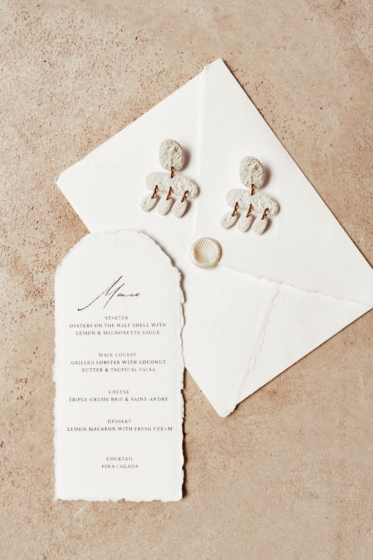 Menu card with shell drop earrings and a deckle-edged envelope