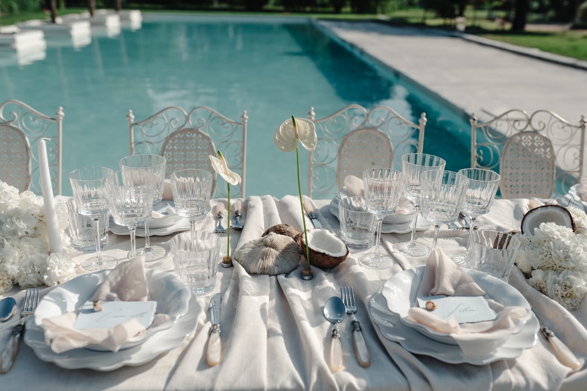 Poolside table setting with coconut shells, white florals and crystal glassware