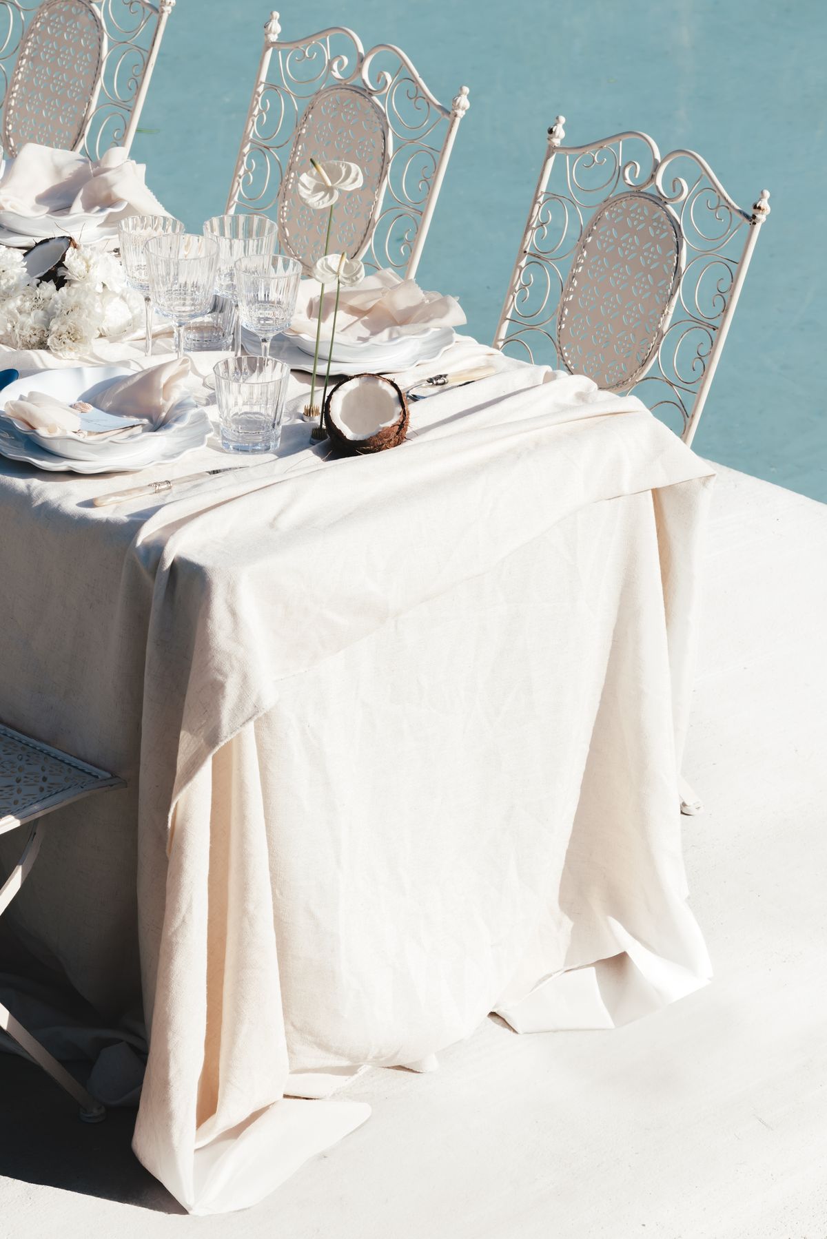 Draped ivory linen and wrought iron seating at the poolside table