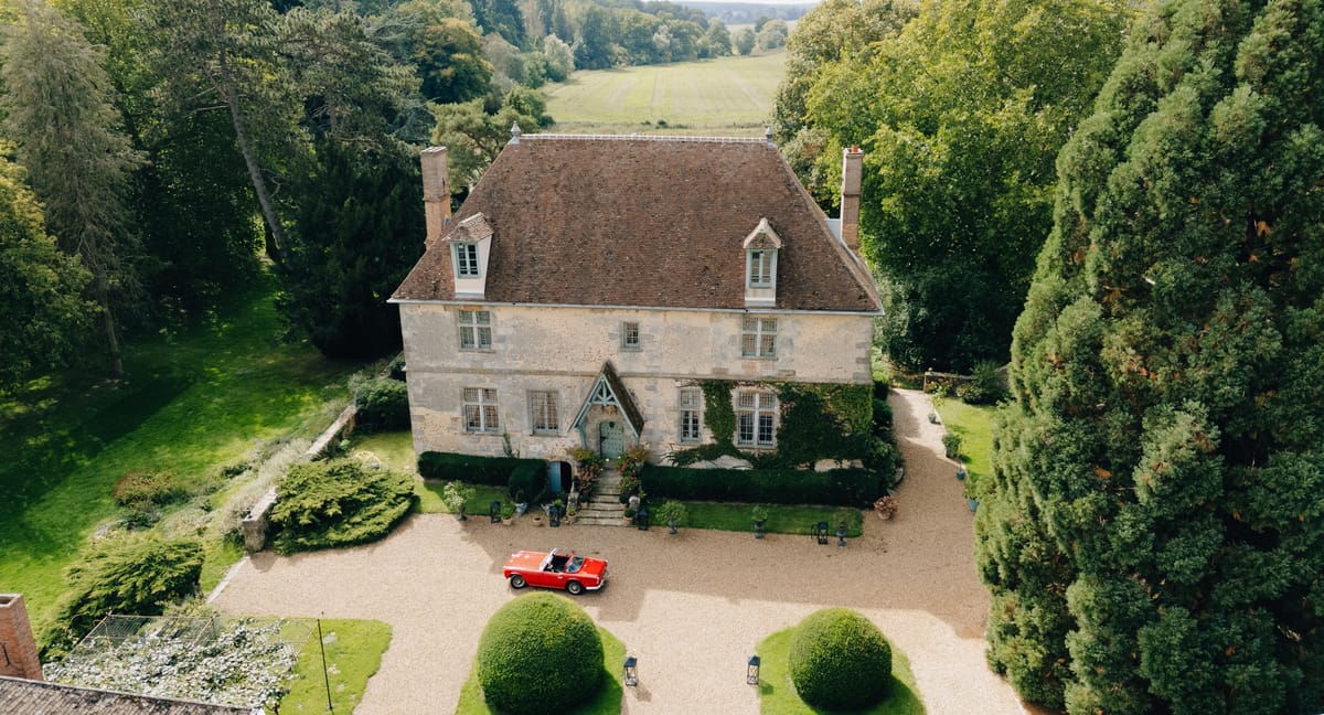 Aerial view of the manor's forecourt with a red vintage convertible parked among the topiary