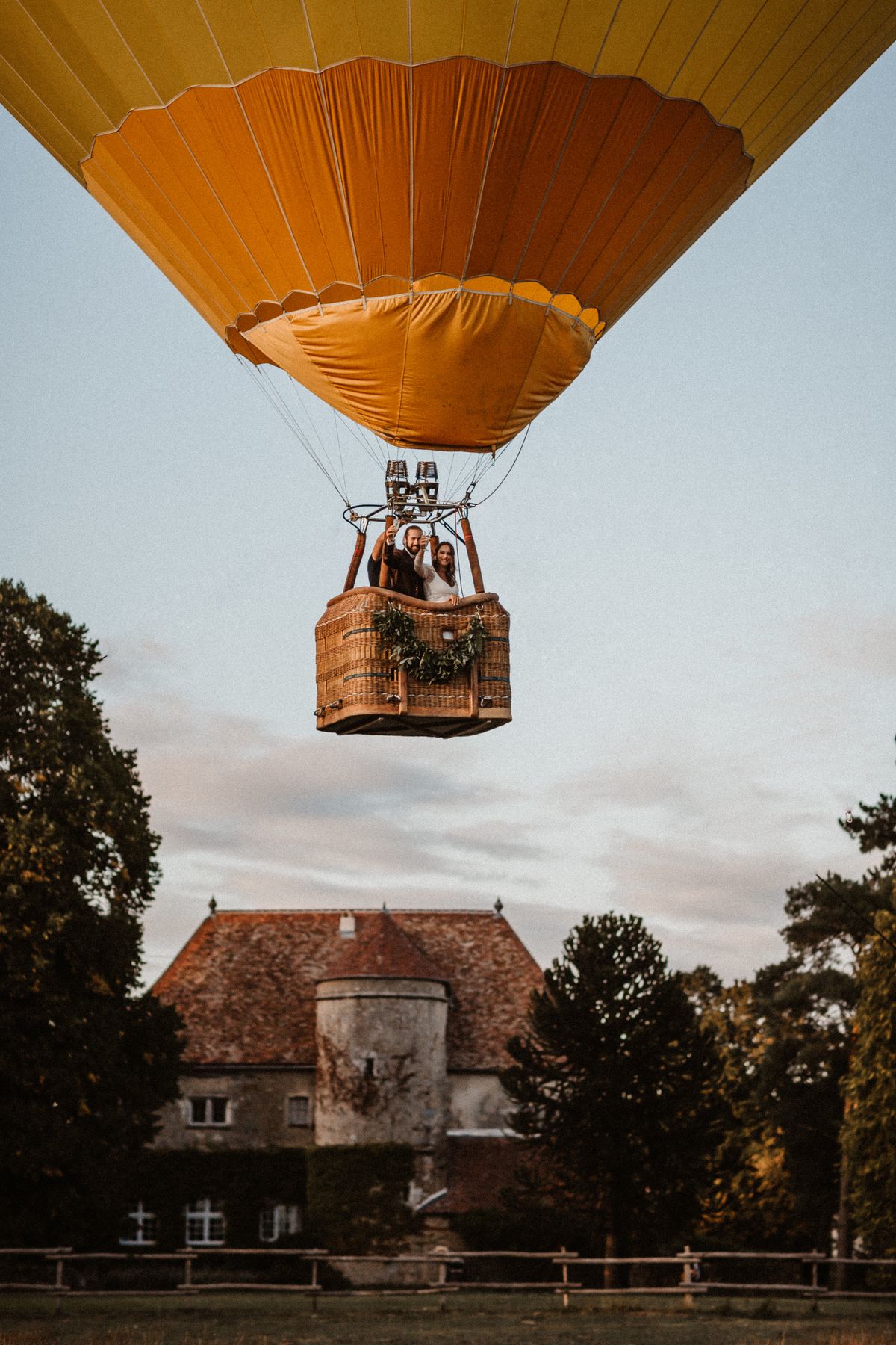 Couple in a hot air balloon basket rising above the manor's grounds