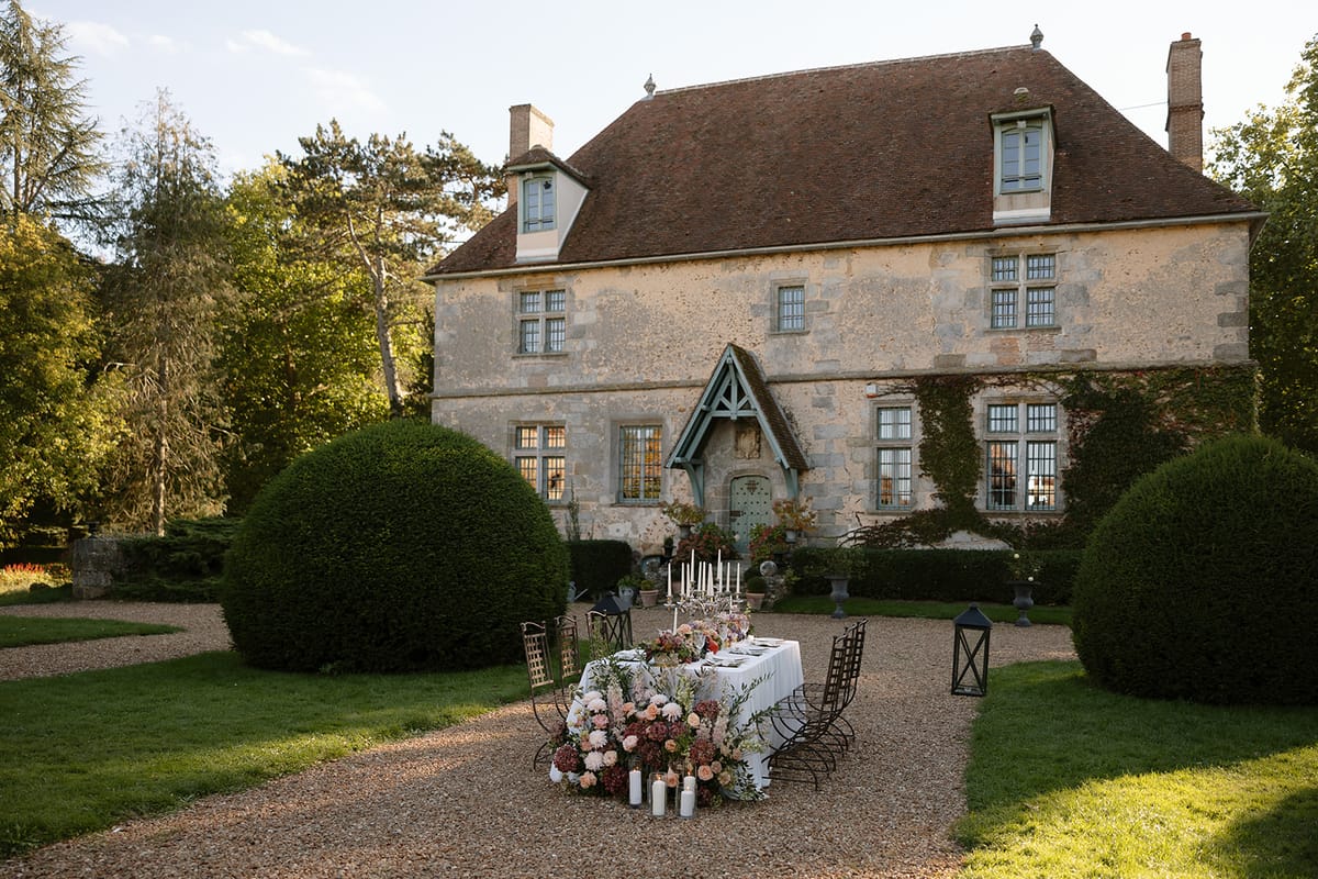 Outdoor reception table set for dinner among candelabras beneath the manor's facade at golden hour