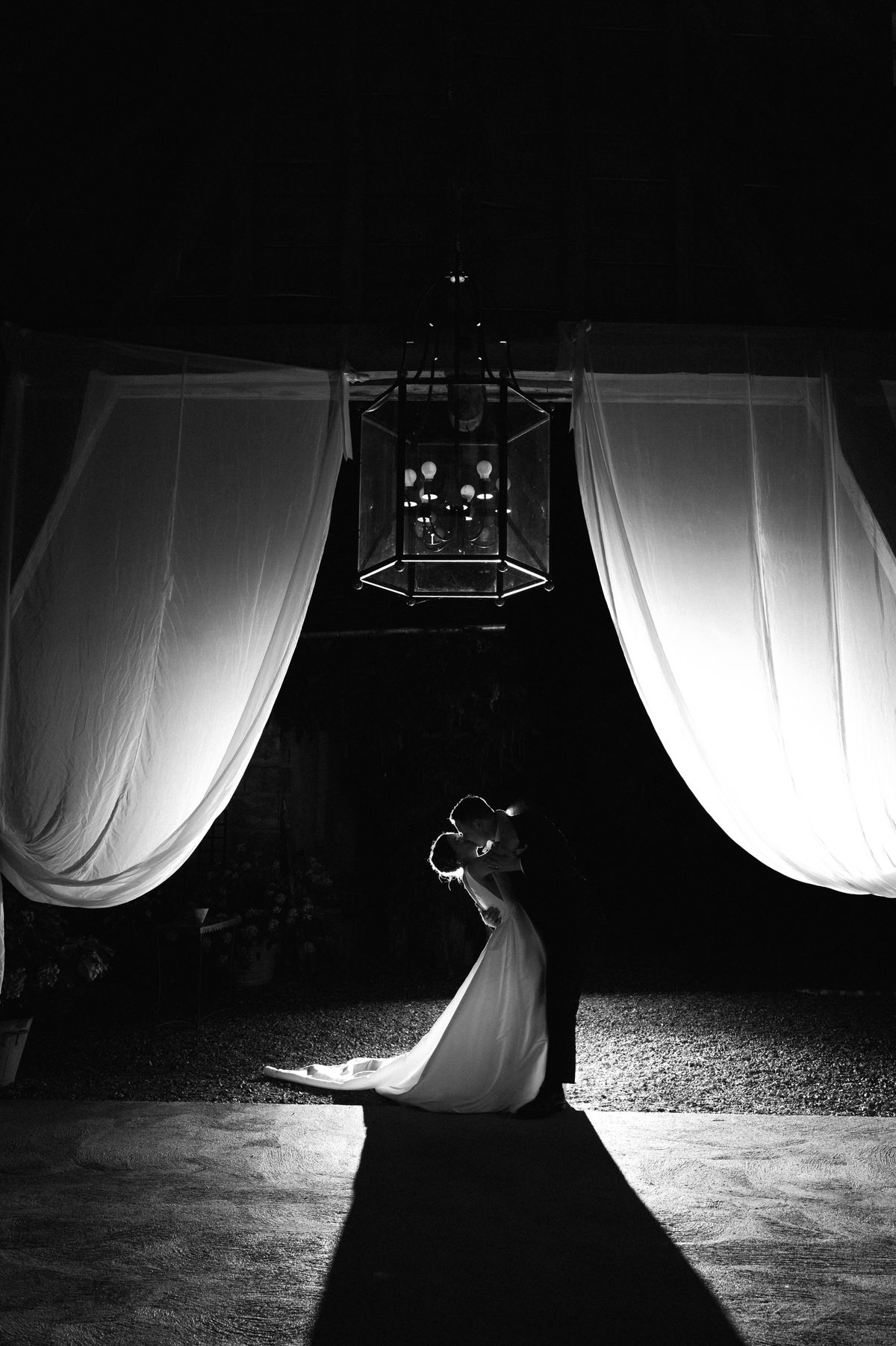 Couple embracing in the reception hall beneath a lantern, framed by sheer curtains