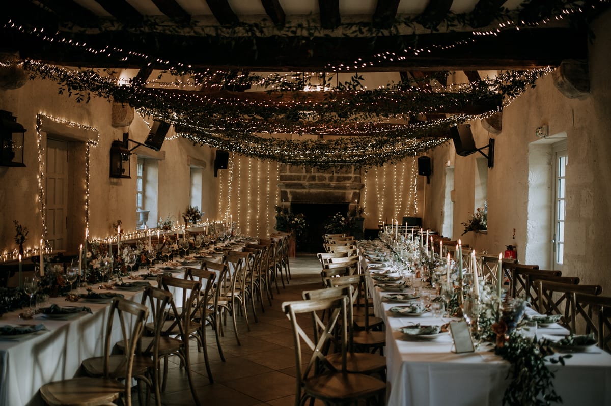Reception hall strung with fairy lights and greenery garlands, tables set for dinner