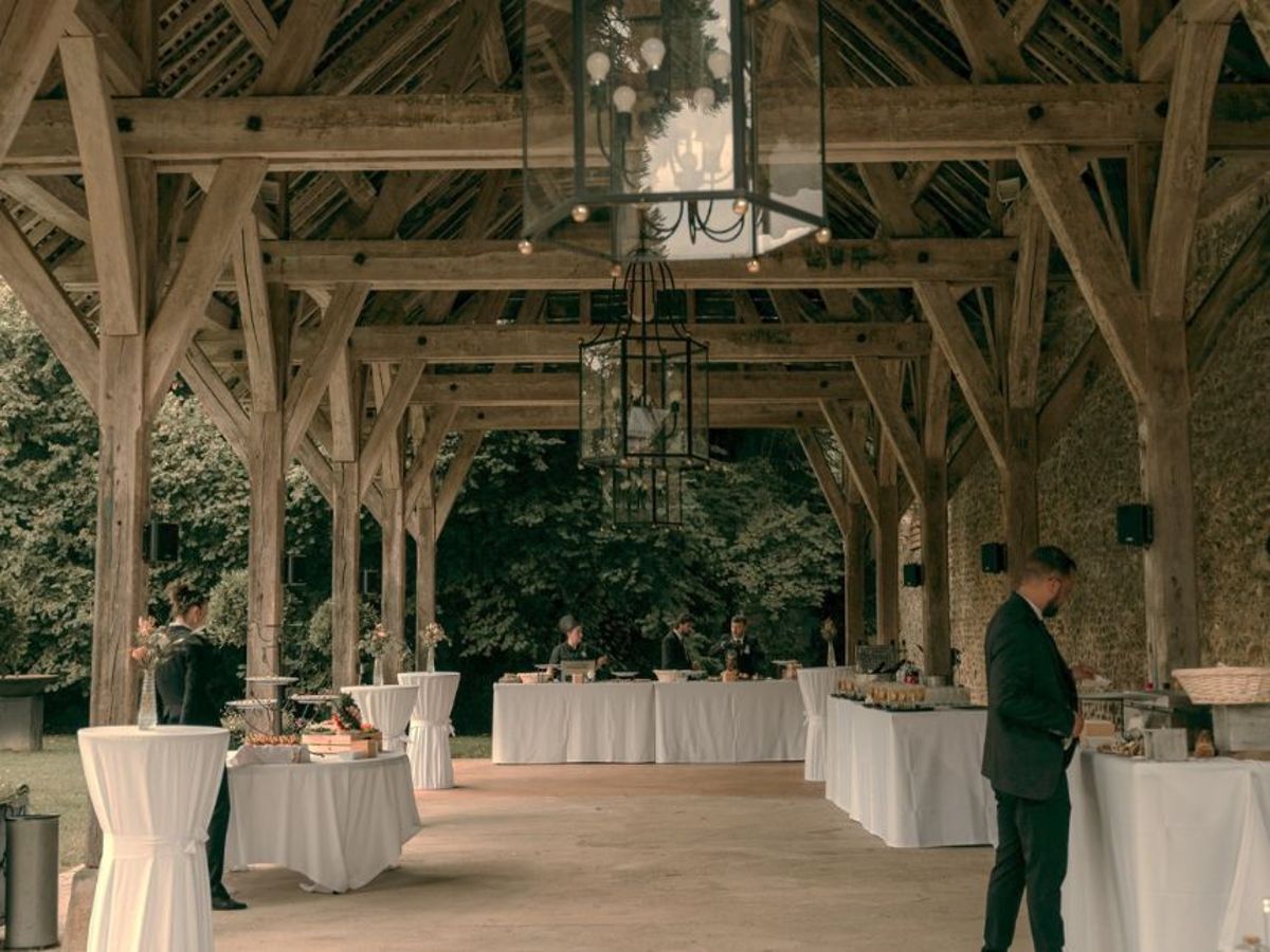 Empty reception hall with long tables, market lights and greenery garlands strung from wooden beams