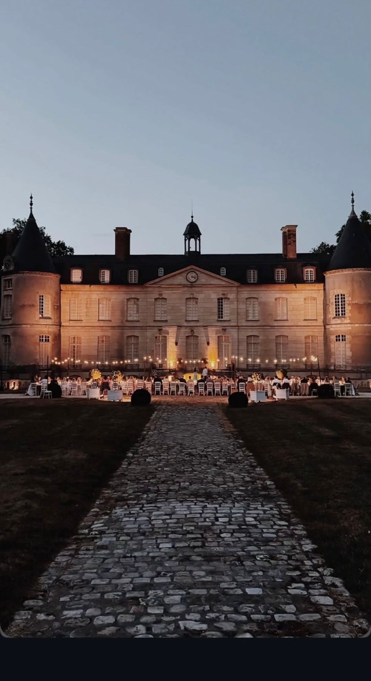 Evening wedding reception dinner in front of the château at Domaine de Verderonne, guests seated under string lighting.
