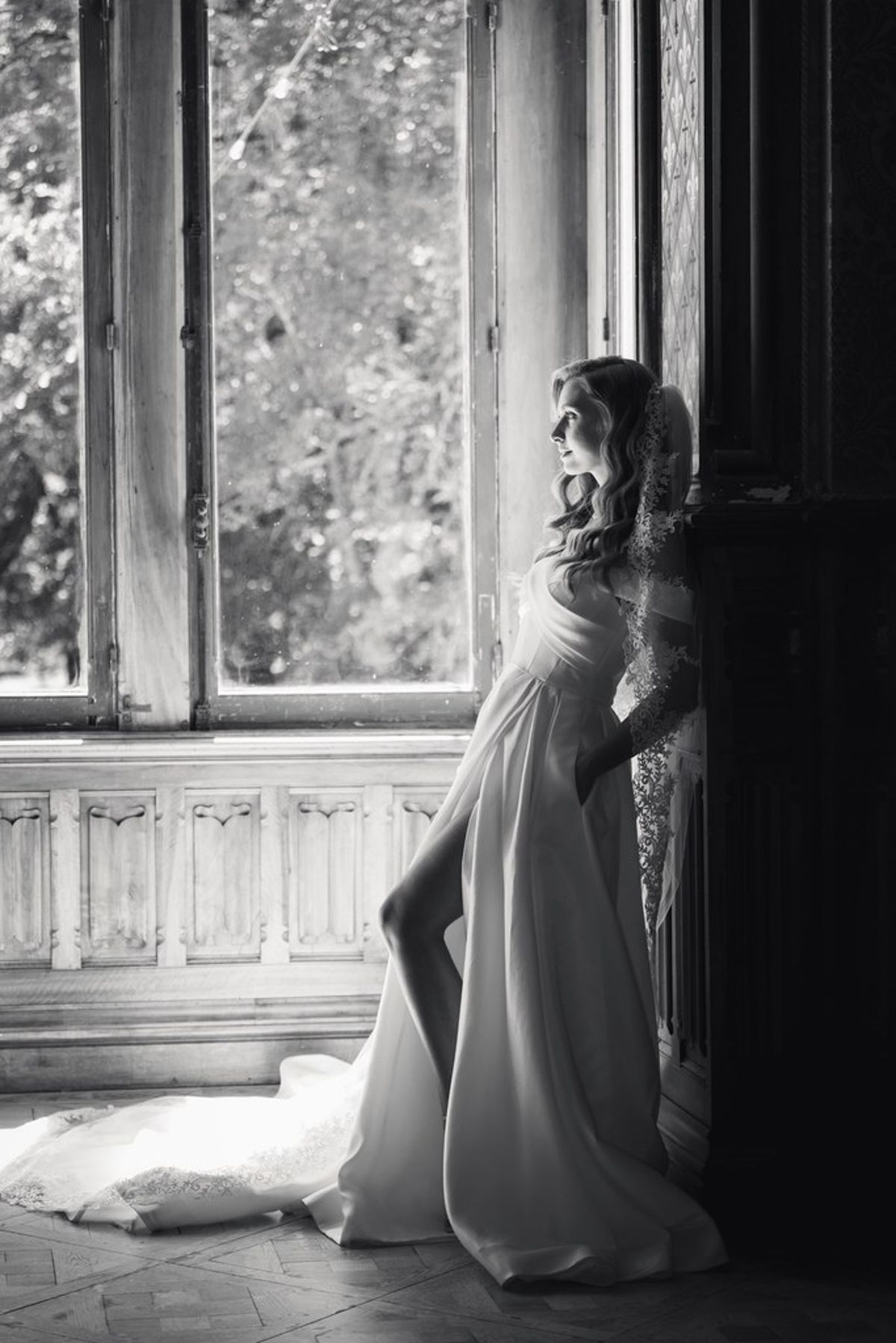Blush and fuchsia styled shoot at Château du Causse, Occitanie, the bride leaning by a tall window, in black and white