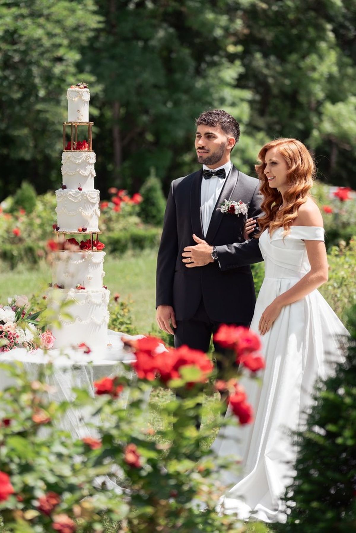 Blush and fuchsia styled shoot at Château du Causse, Occitanie, the couple beside a tiered white cake among red roses