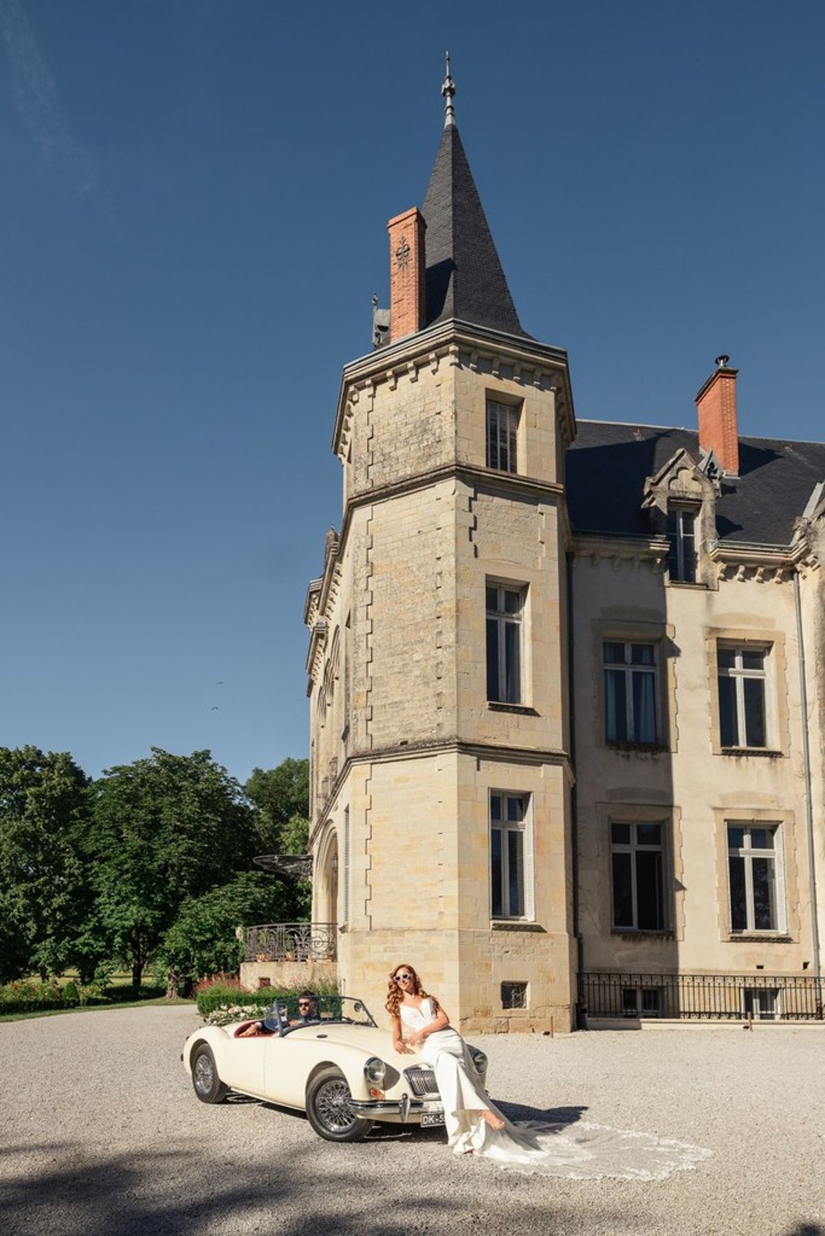Blush and fuchsia styled shoot at Château du Causse, Occitanie, the bride on the vintage car in front of the château tower