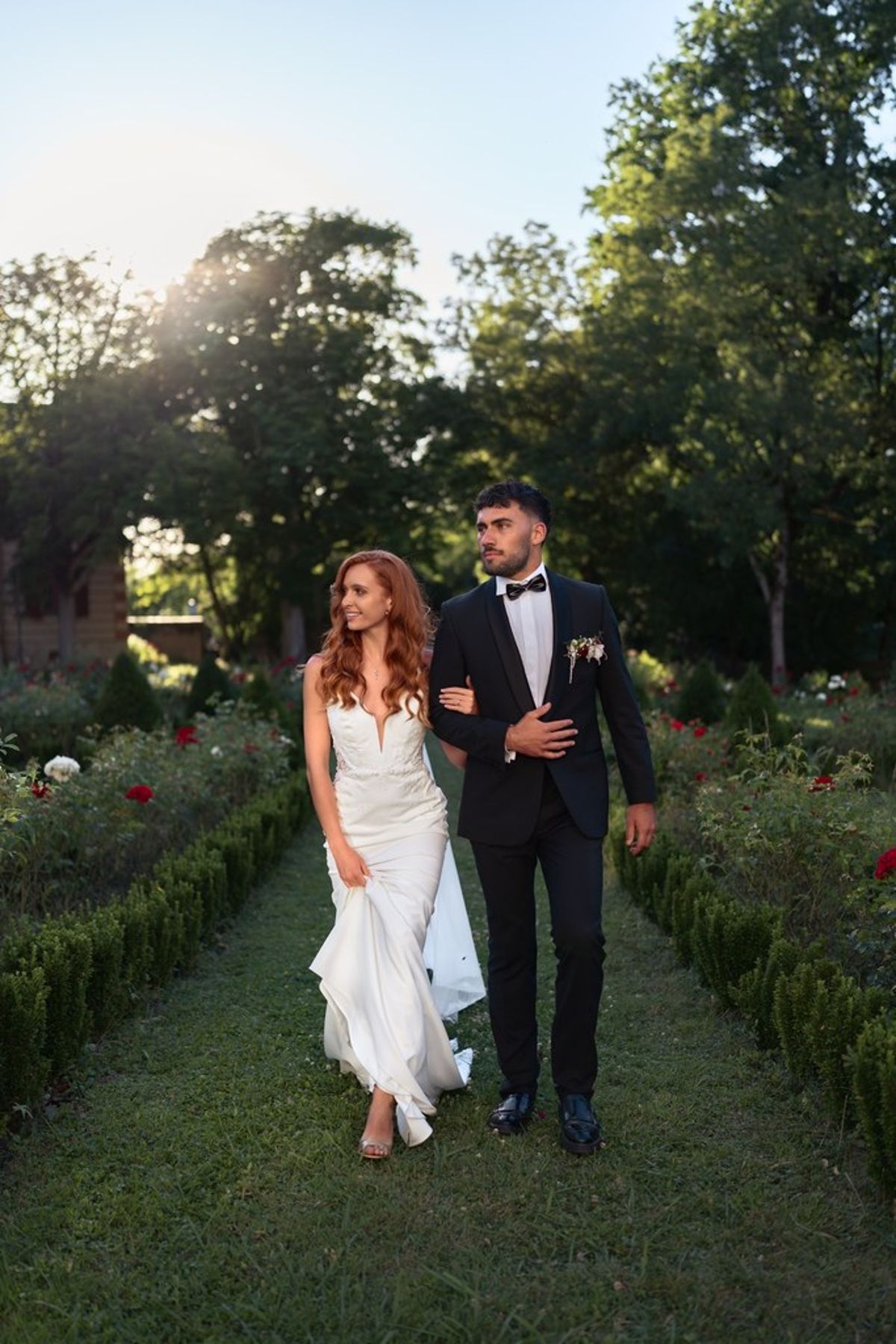 Blush and fuchsia styled shoot at Château du Causse, Occitanie, the couple walking arm in arm along a hedged garden path
